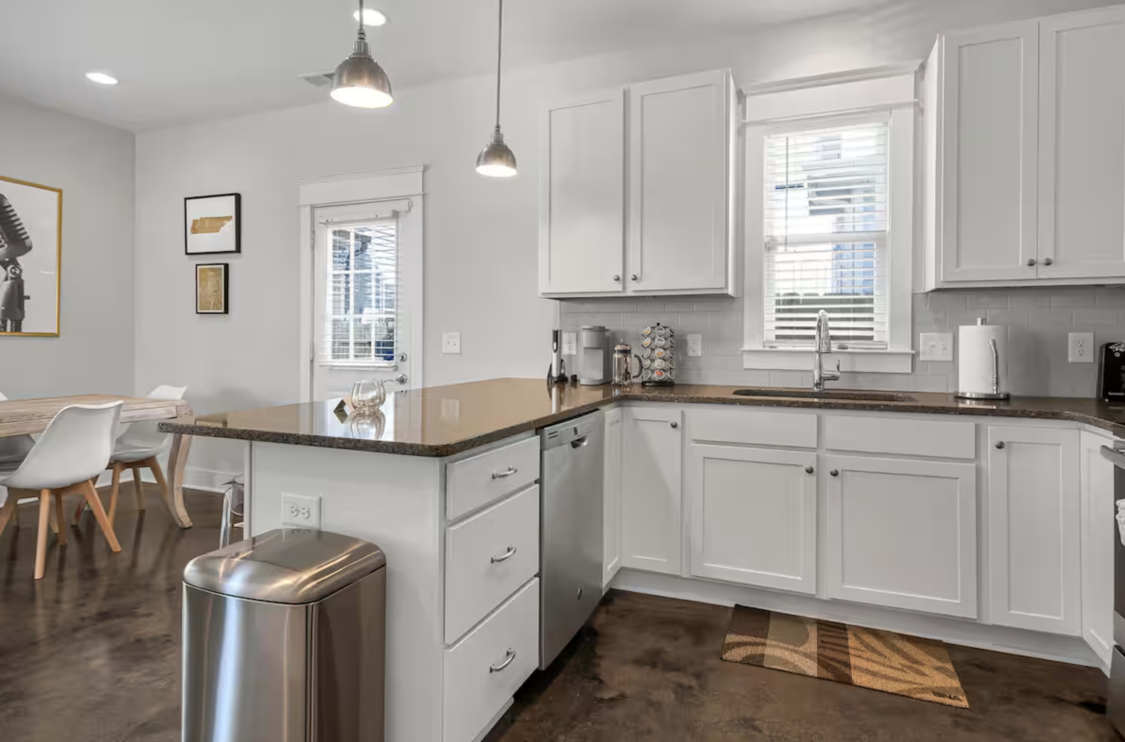 The kitchen features white cabinets, a dark countertop, and stainless steel appliances, with a dining area visible in the background.
