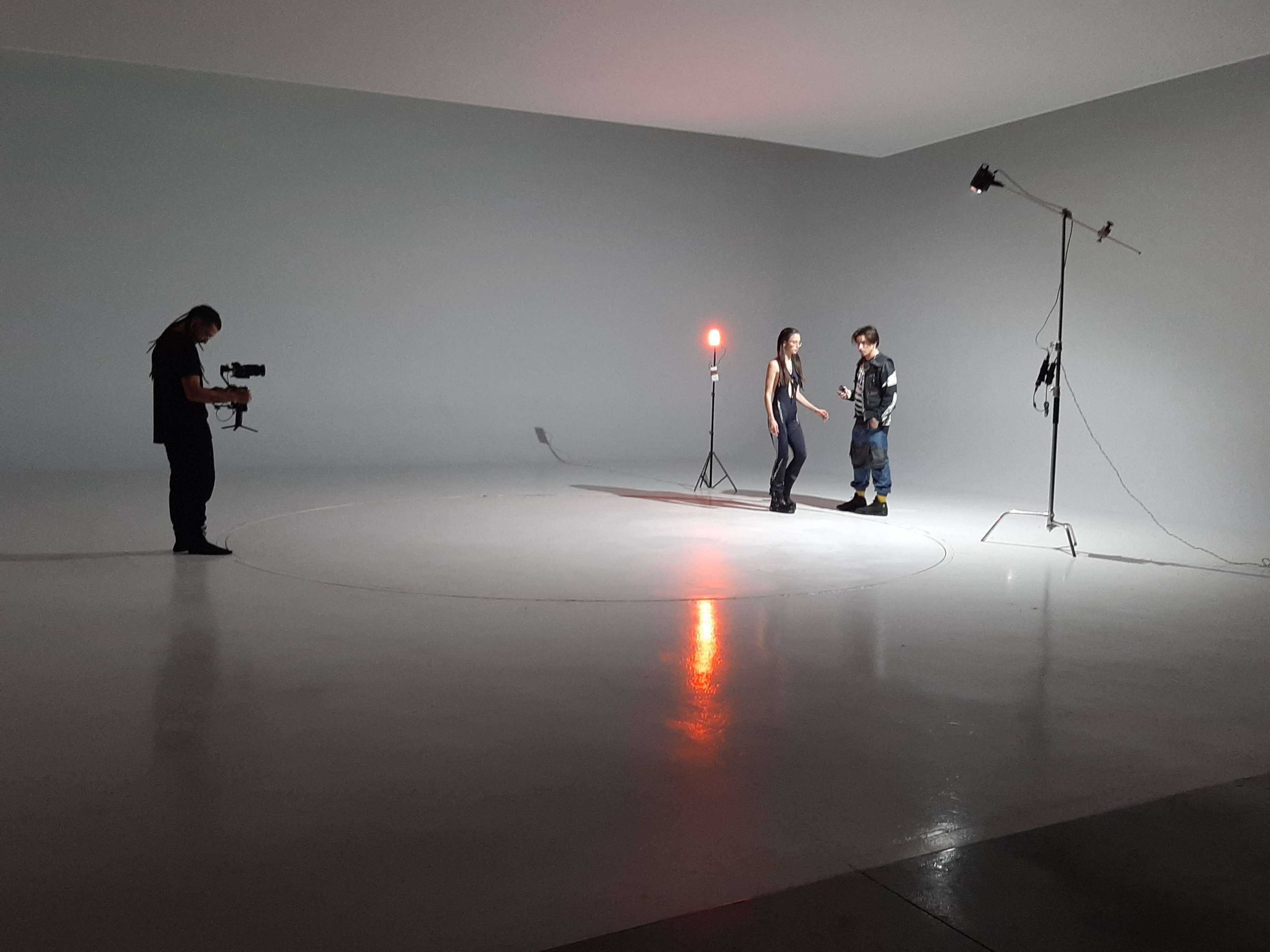 A photographer captures two people engaged in a conversation in a minimally lit studio space.