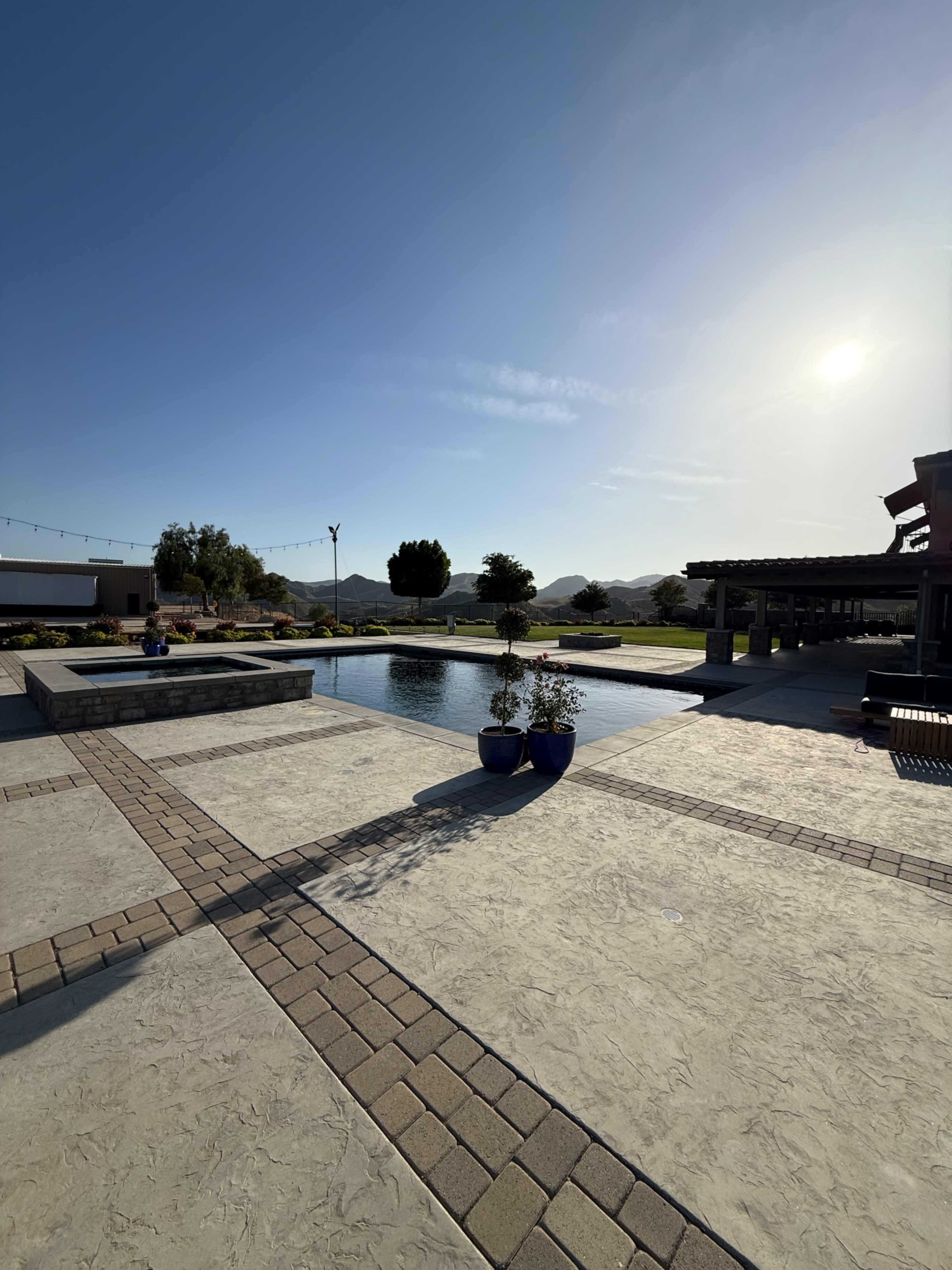 The image shows a landscaped outdoor area with a pool, surrounding planters, and distant mountains under a clear sky.