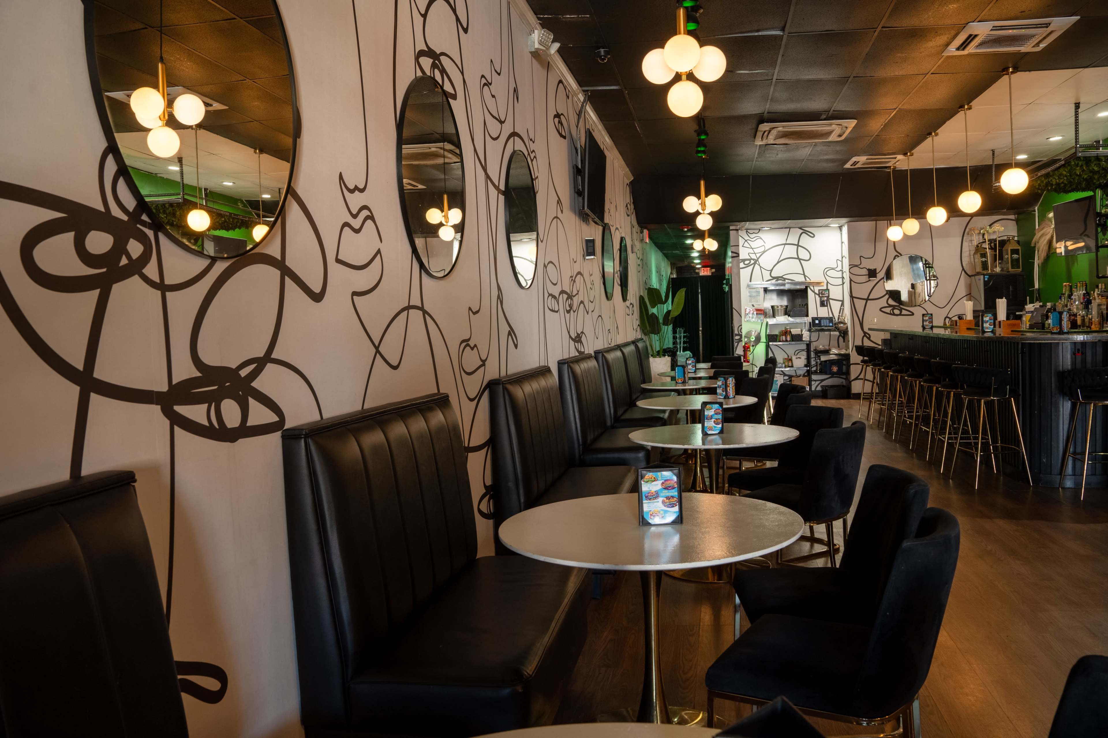 The image shows a modern café interior with black seating, round tables, and artistic line drawings on the walls, illuminated by pendant lights.