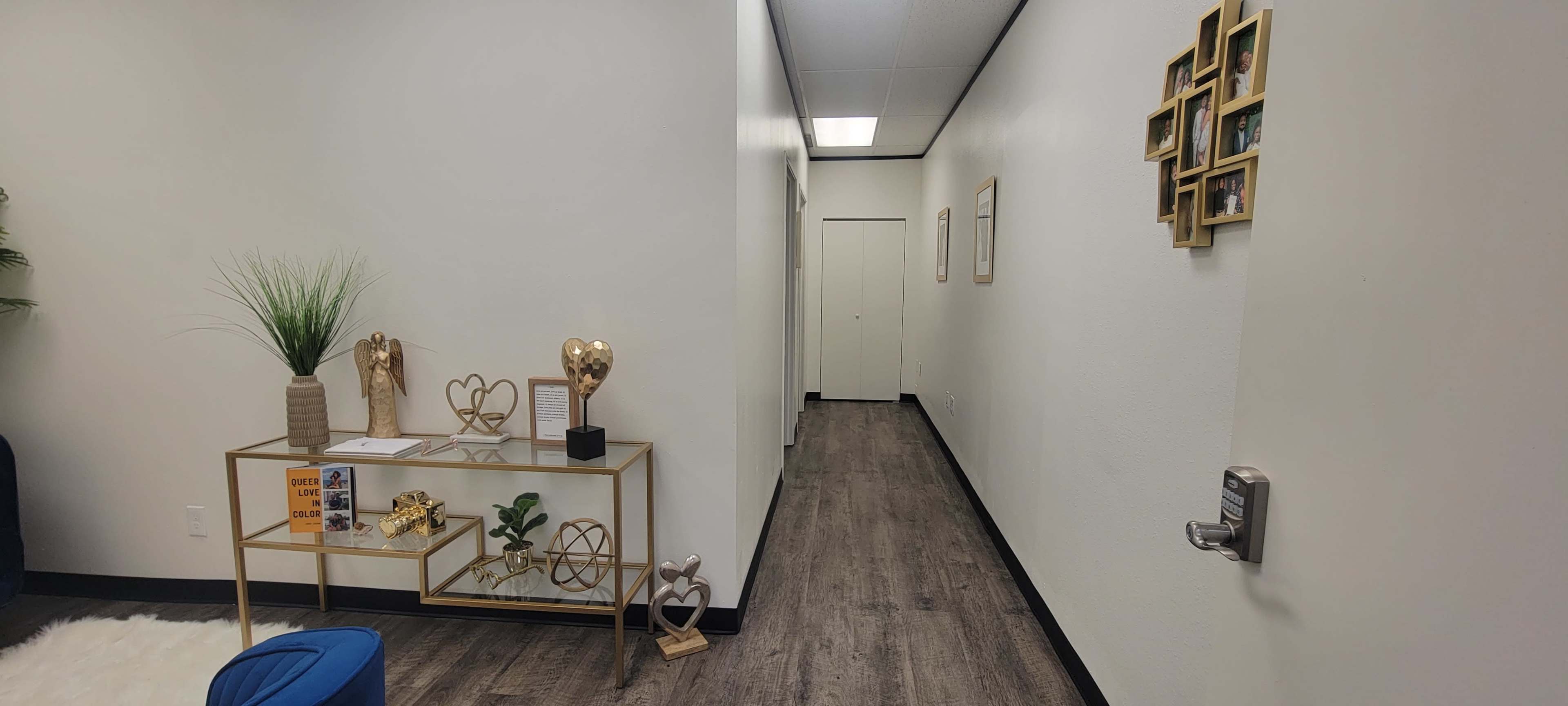 A narrow hallway with white walls, wooden flooring, and decor items on a gold table to the left.