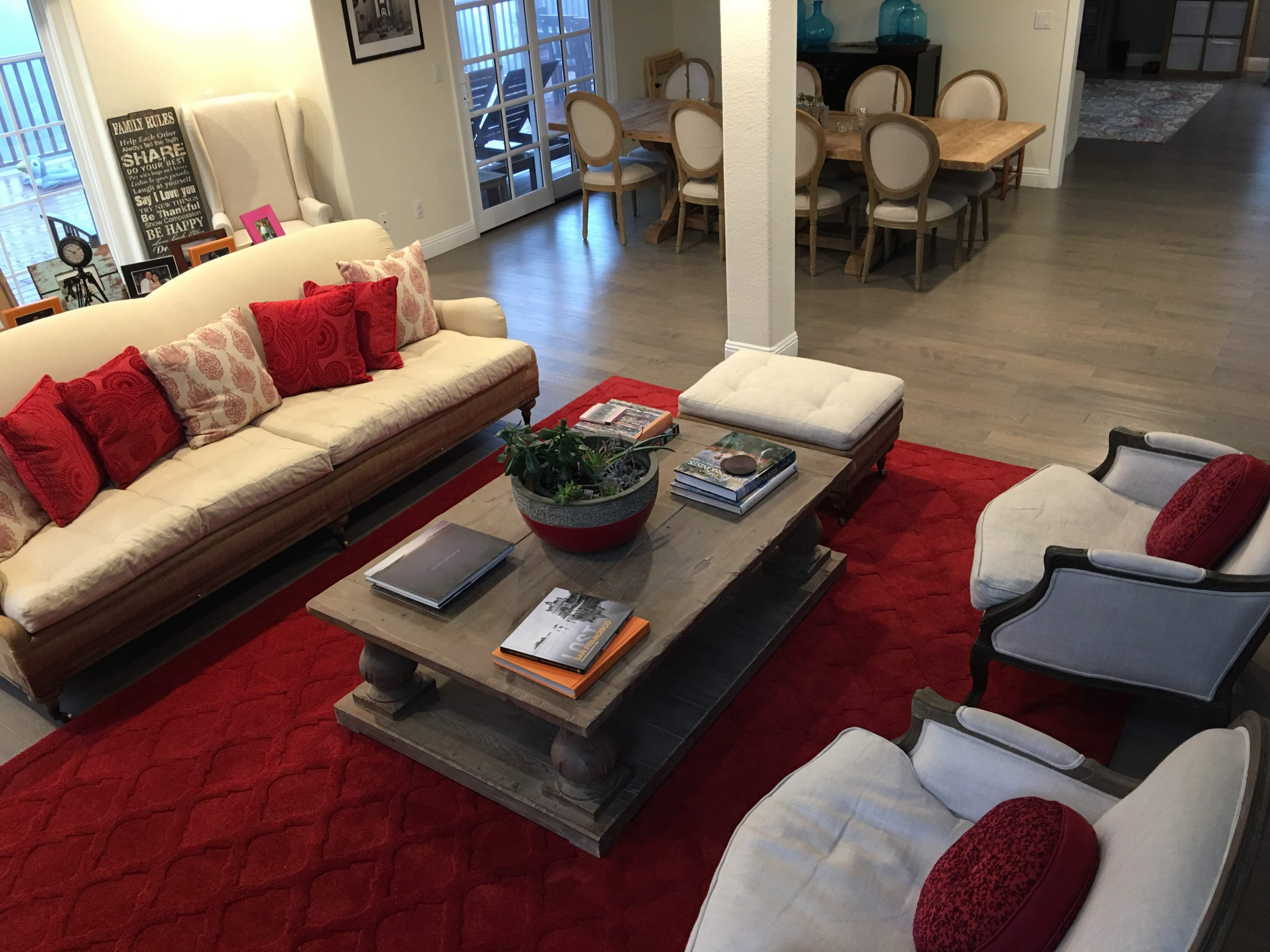 A living room featuring two sofas with red cushions, a wooden coffee table with books and a plant, and two armchairs, all situated on a red area rug.