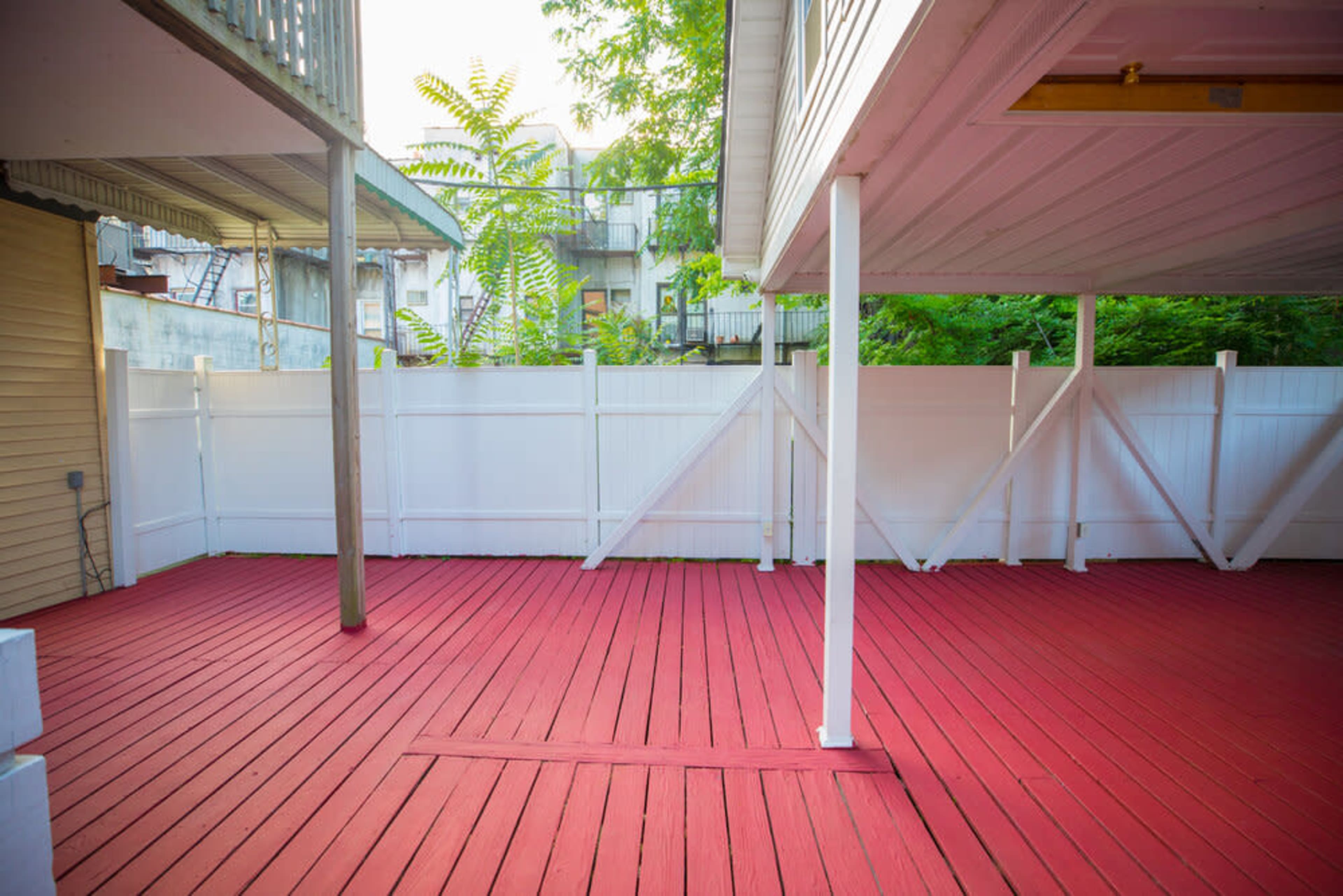 A red-painted wooden deck enclosed by a white wooden fence and surrounded by greenery.