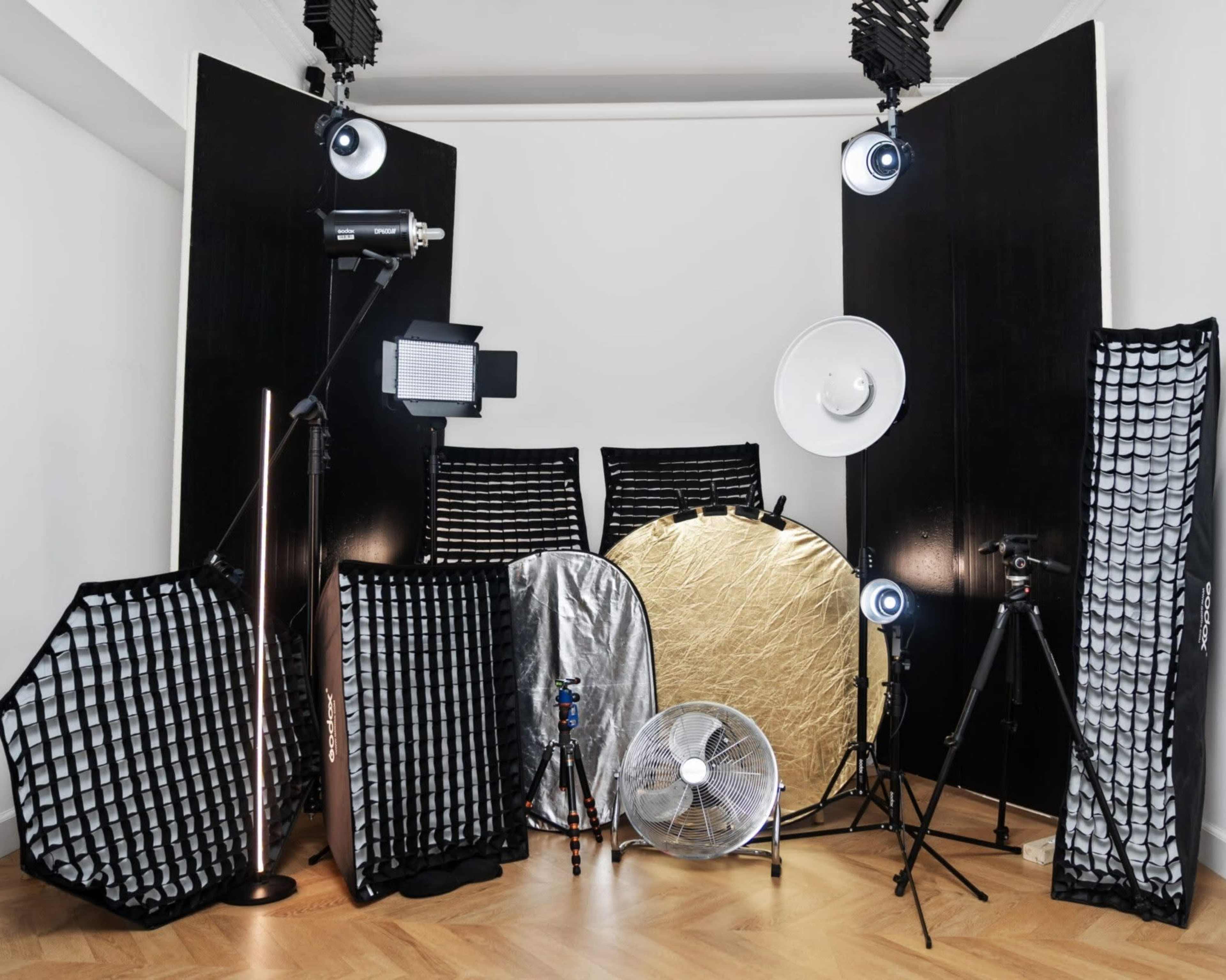 The image shows a photography studio setup featuring various lighting equipment, reflectors, and a fan arranged around a tripod.