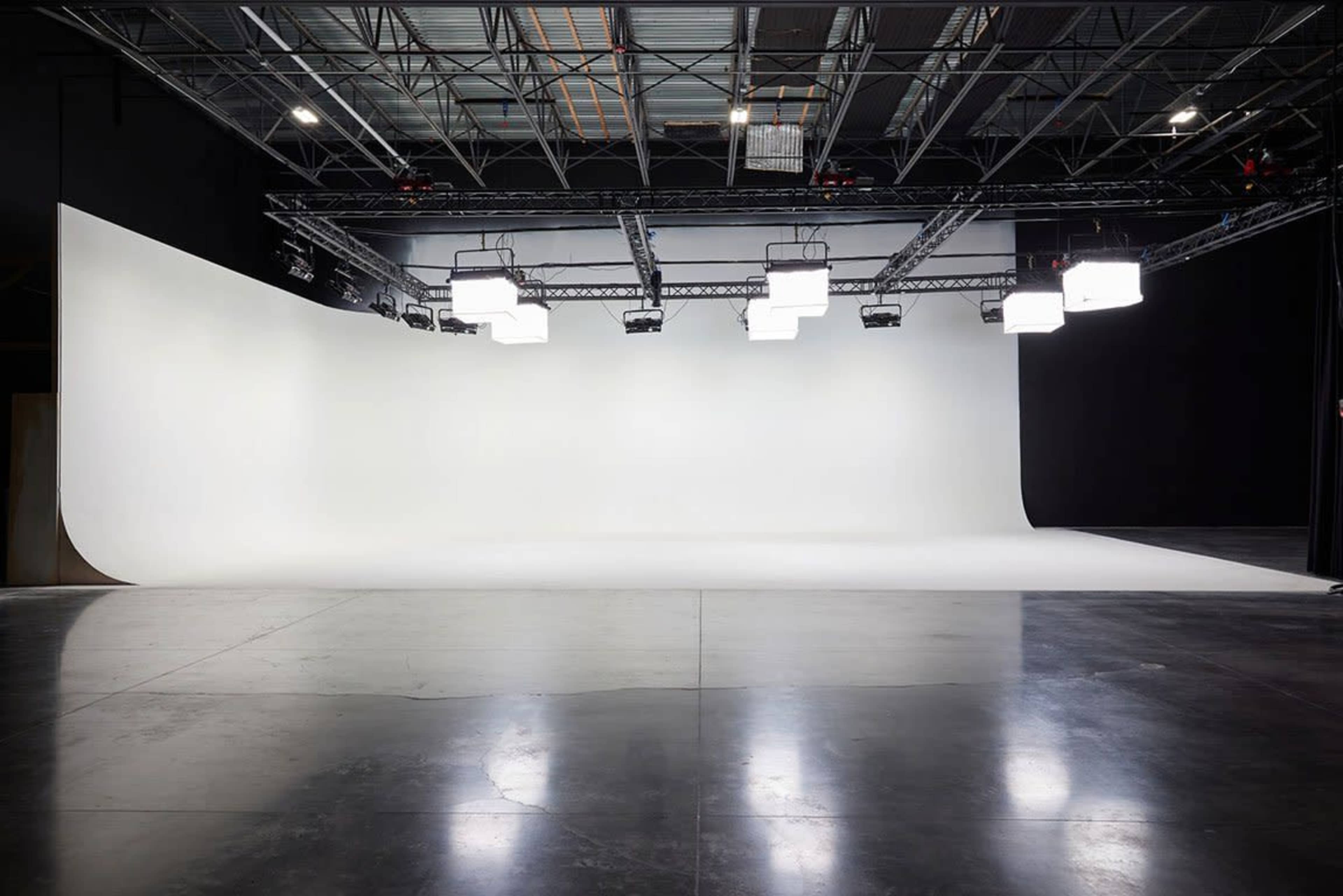 A spacious photography studio with a curved white backdrop and overhead lights.