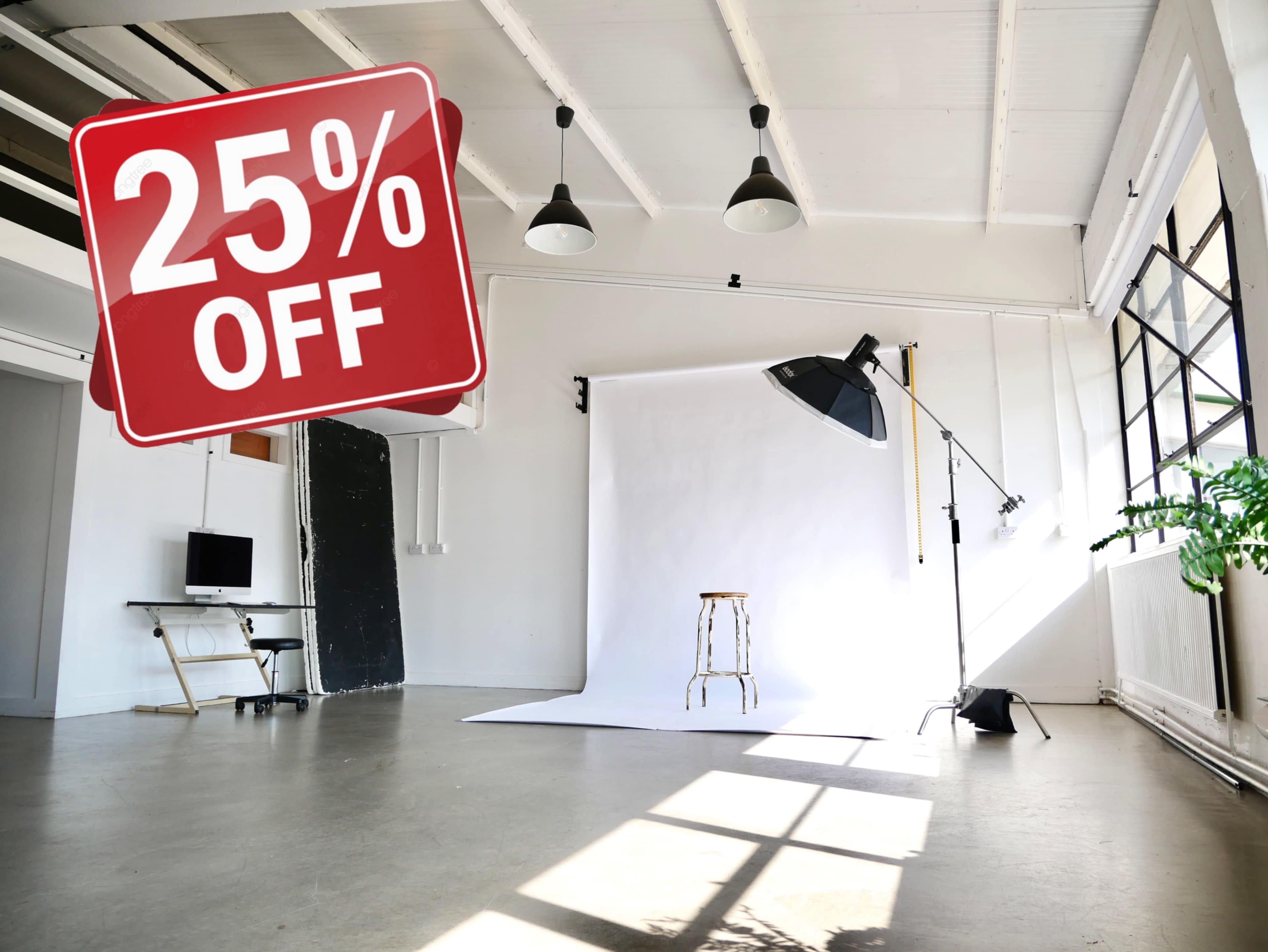 The image shows a spacious photography studio with a white backdrop, a stool, lighting equipment, and a promotional sign indicating a 25% discount.