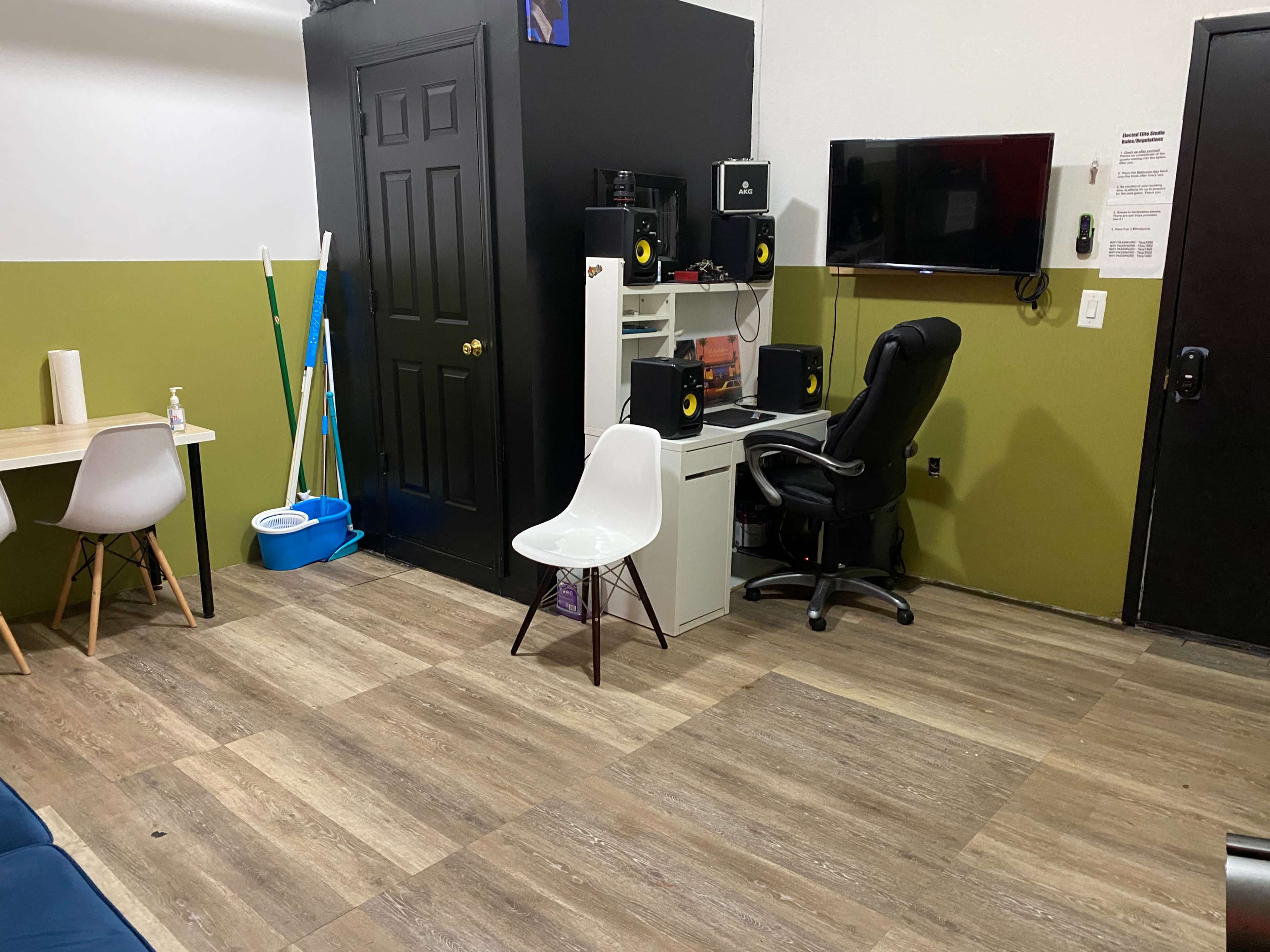 The image shows a room with a sectional couch, a table, a chair, a desk with speakers, and two doors.