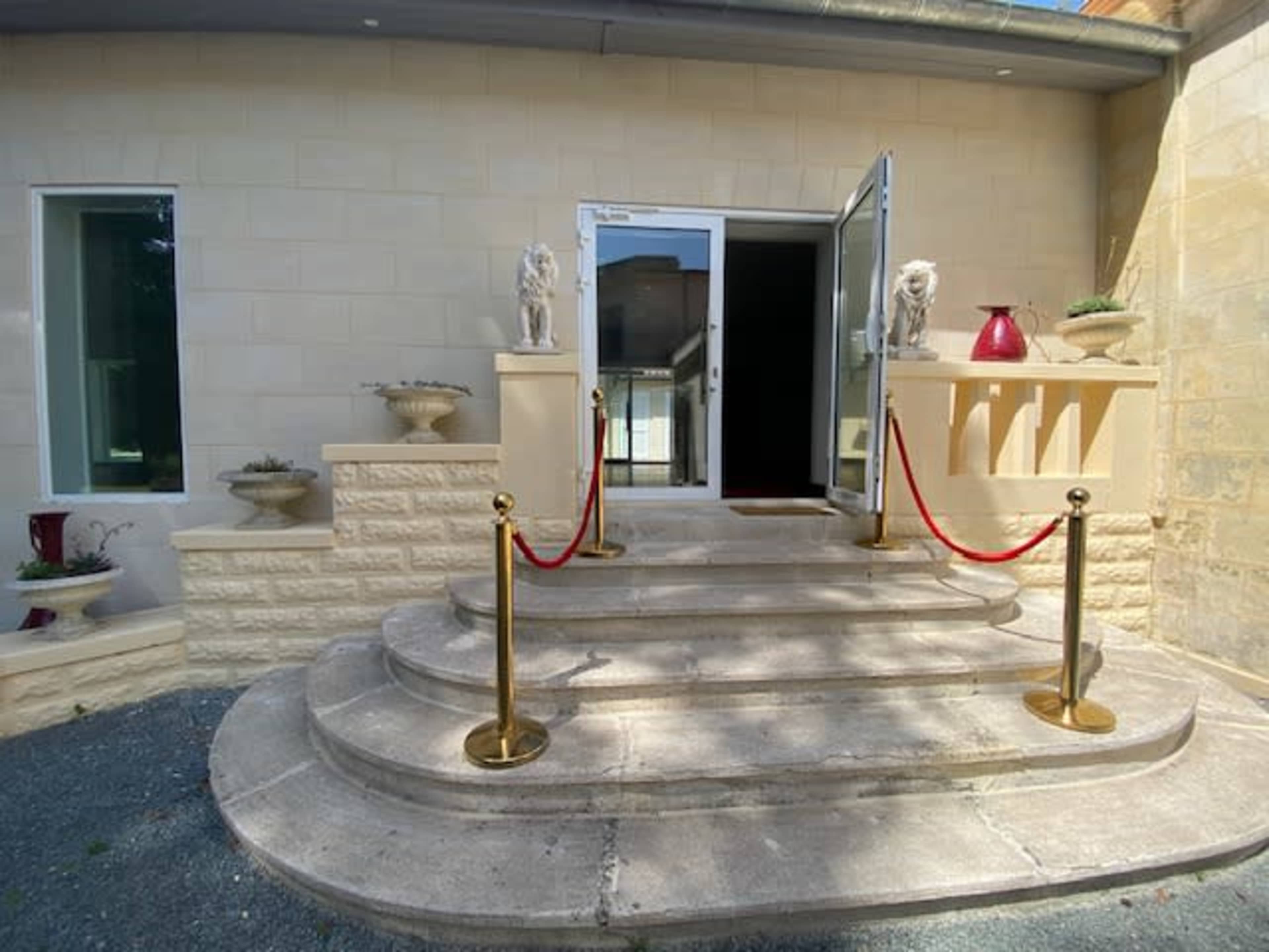 The entrance features a set of stone steps leading to a double door, adorned with lion statues and red ropes separating the area.