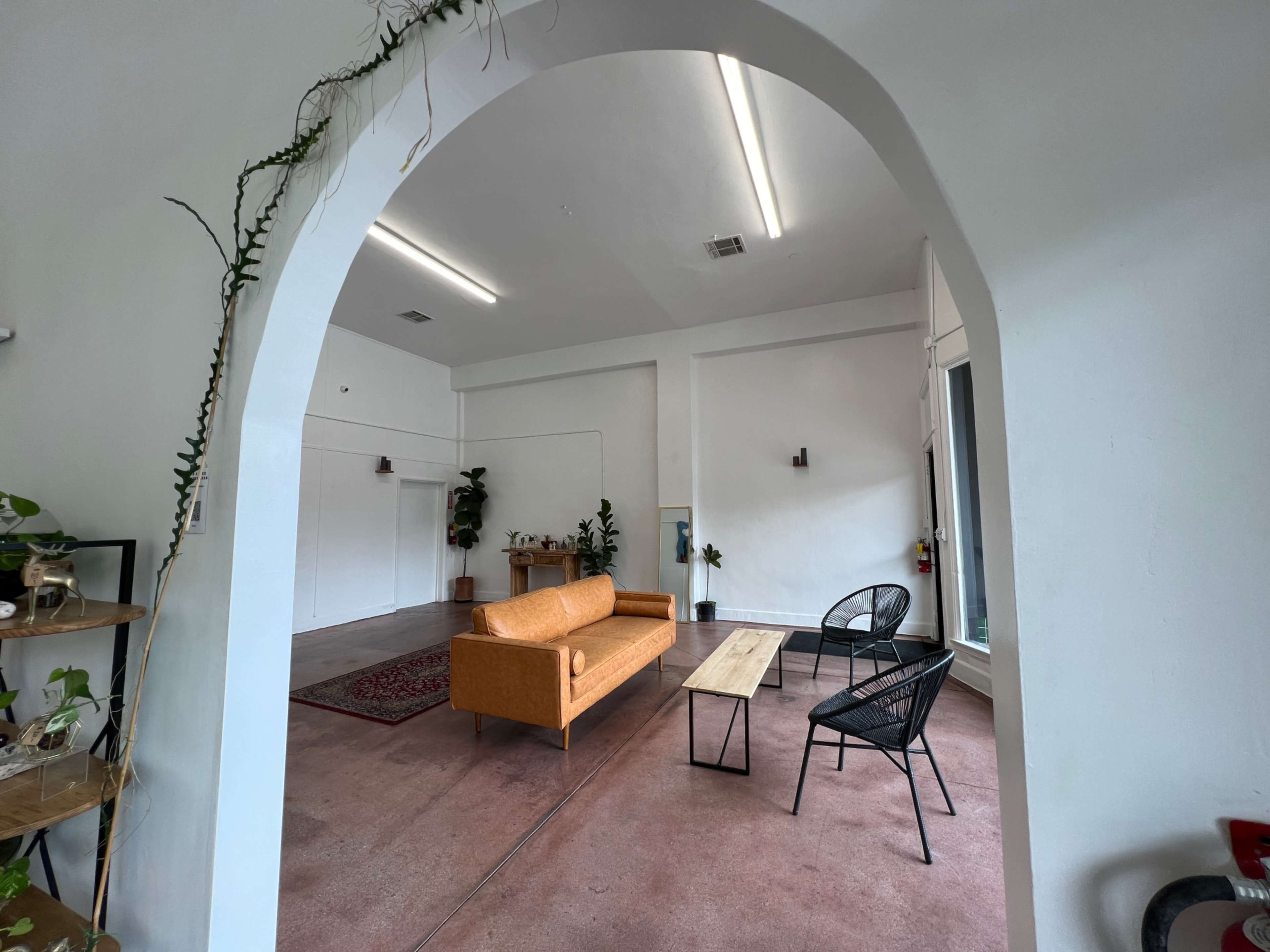 A spacious room with an orange couch, a wooden table, and two black chairs, framed by an archway.