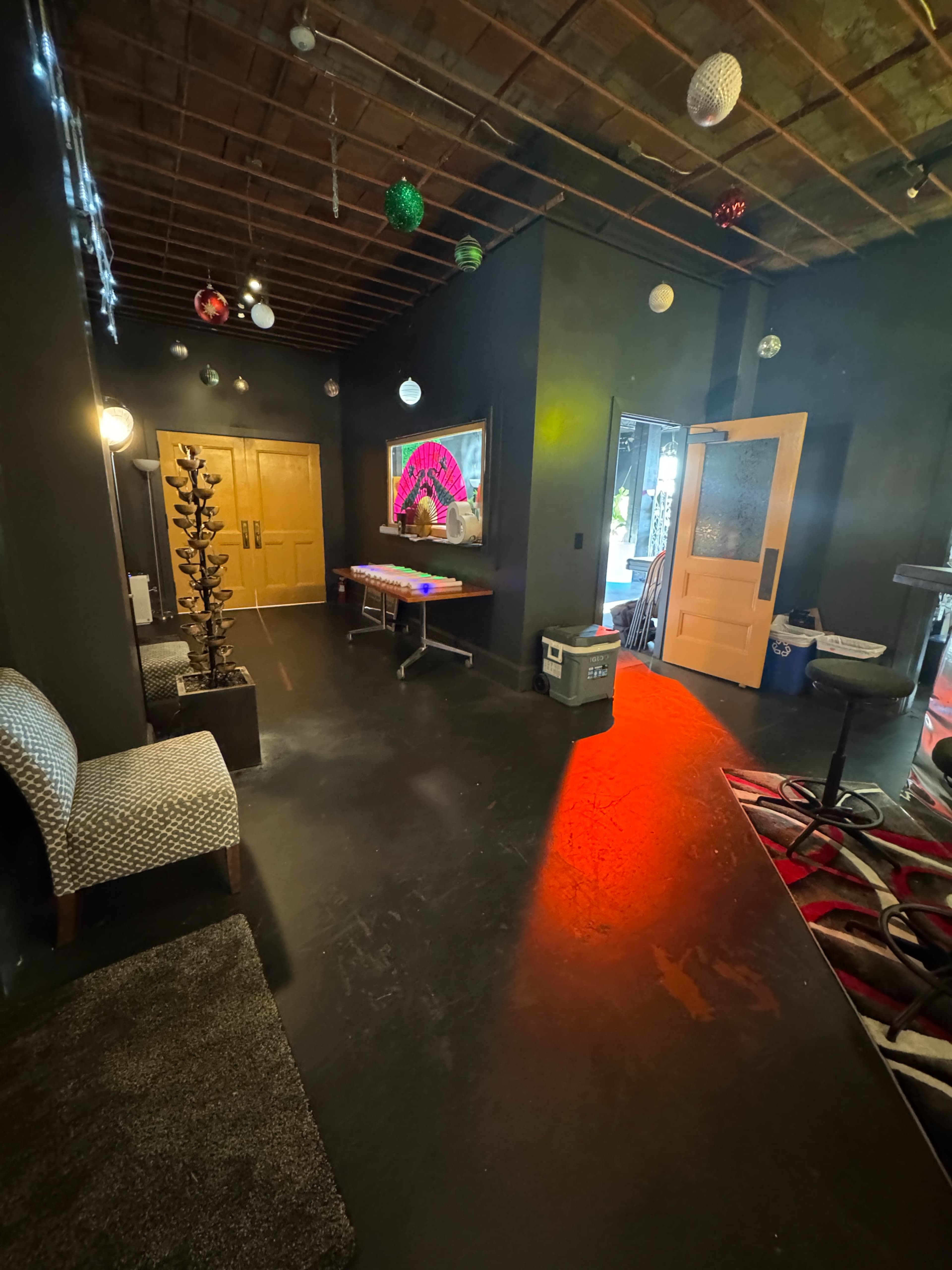 The image shows a dimly lit hallway with a seating area on the left, a television displaying colorful visuals at the end, and a doorway leading outside on the right.