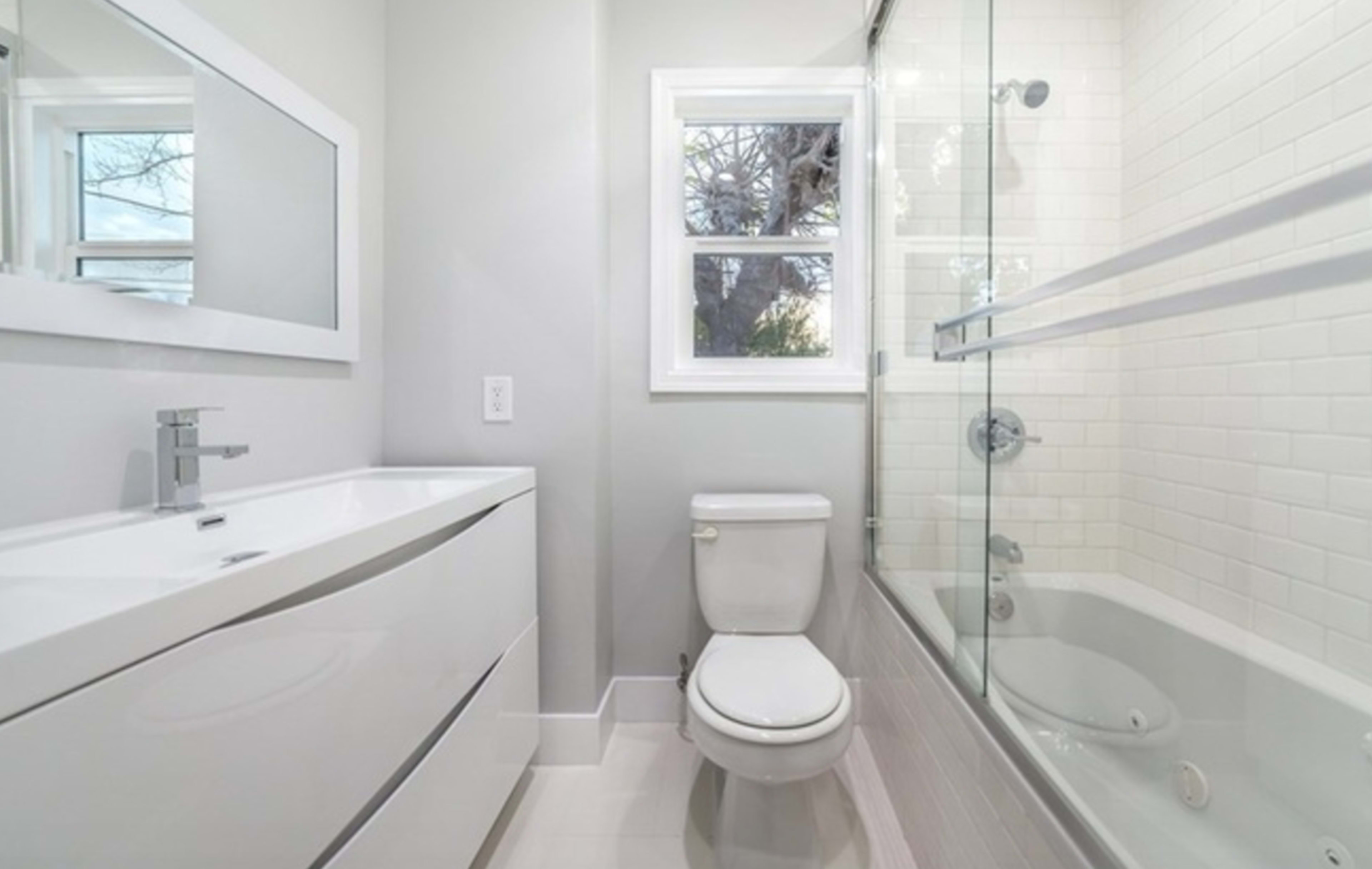 A modern bathroom featuring a glass shower enclosure, a white bathtub, a toilet, and a floating vanity with a sink.