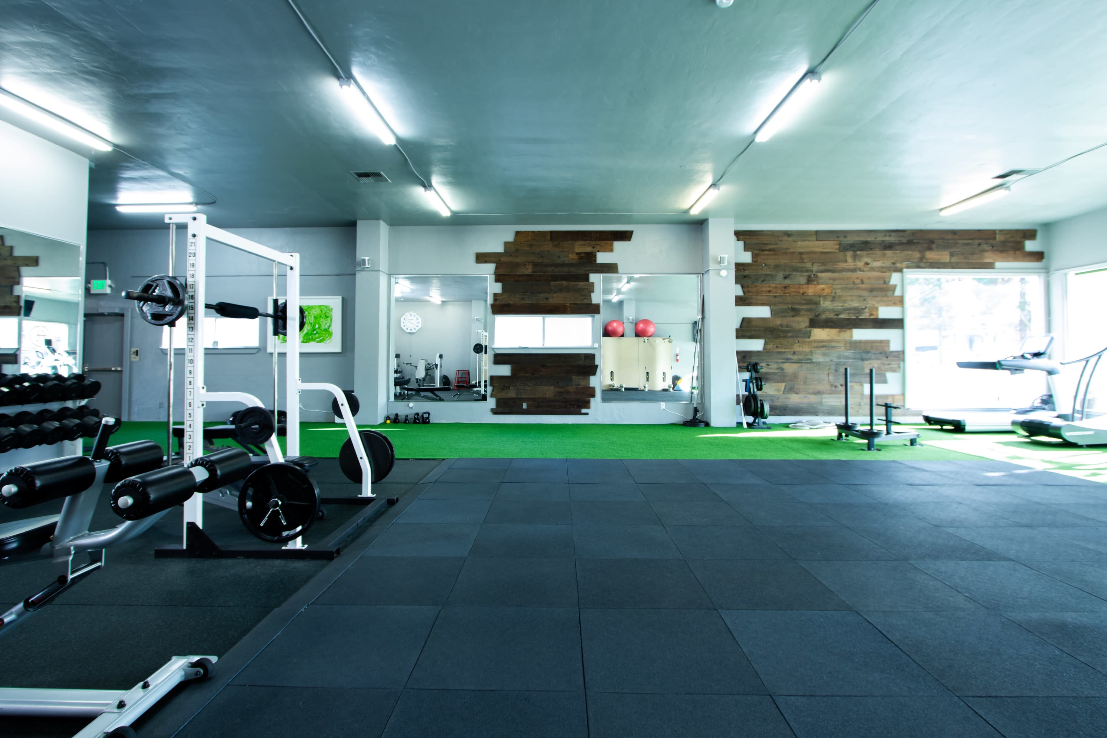 A spacious gym with weightlifting equipment, exercise machines, and a green turf area.