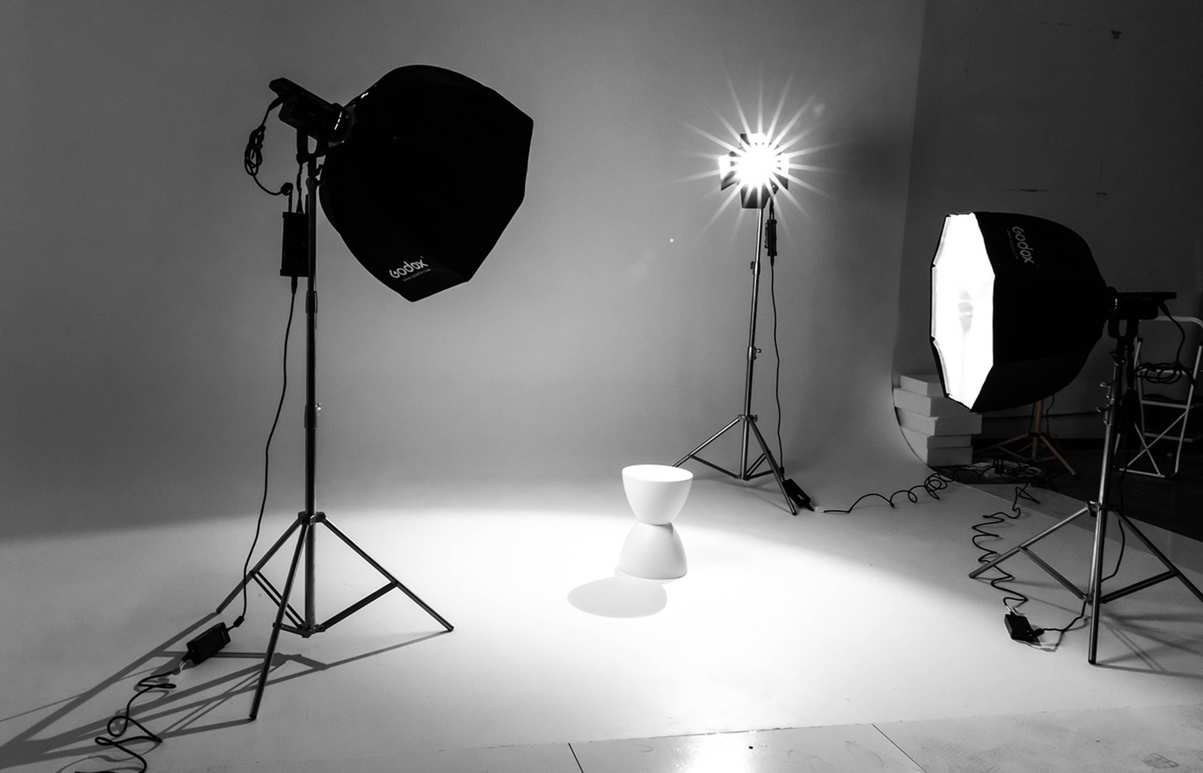 A minimalist photography studio setup with two softbox lights positioned around a small white stool on a plain background.