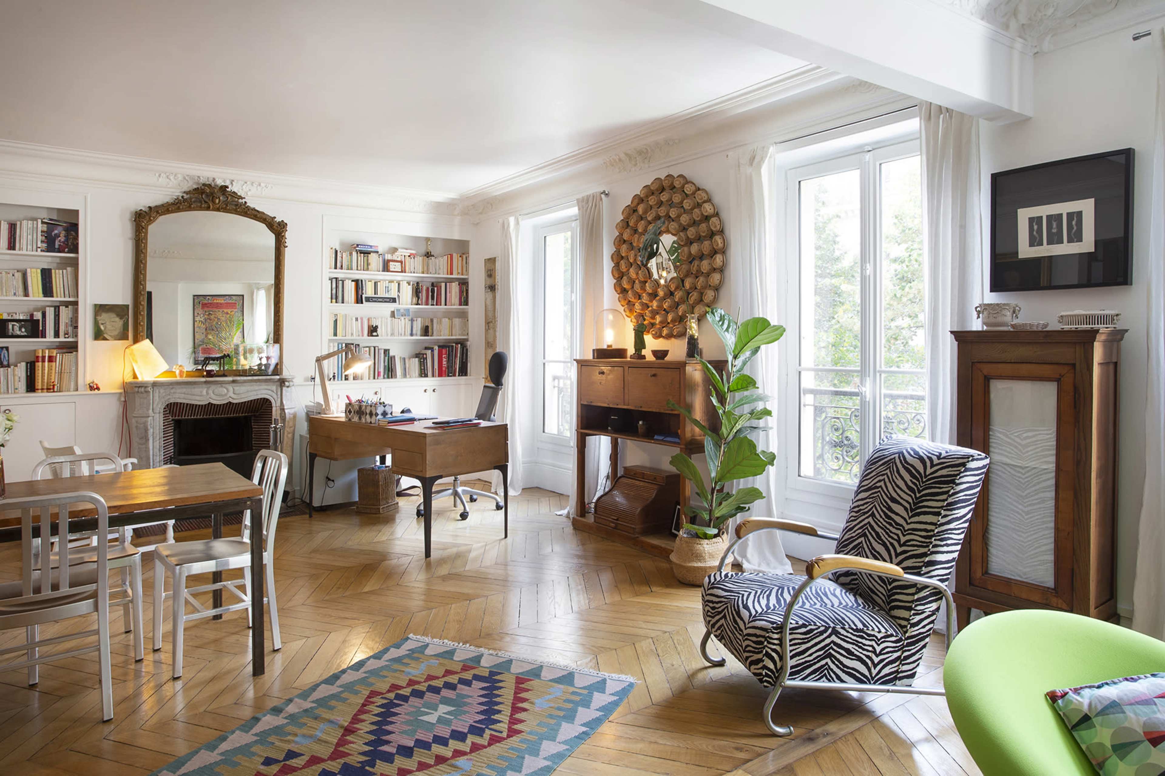 A bright and organized living room featuring a wooden desk, bookshelves, and a mix of modern and vintage furniture.