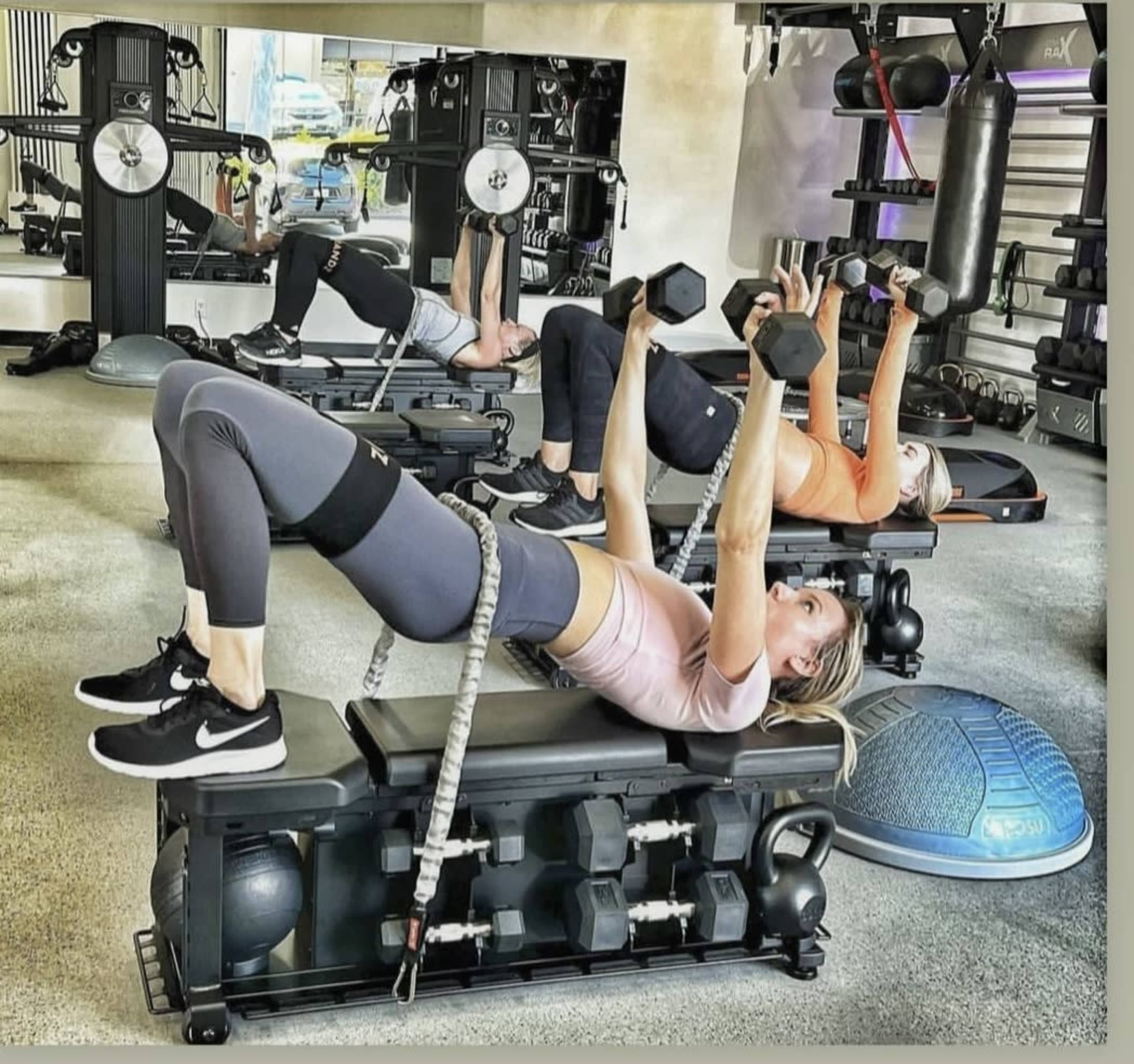 Three individuals perform exercises on benches in a gym, using dumbbells and resistance bands.