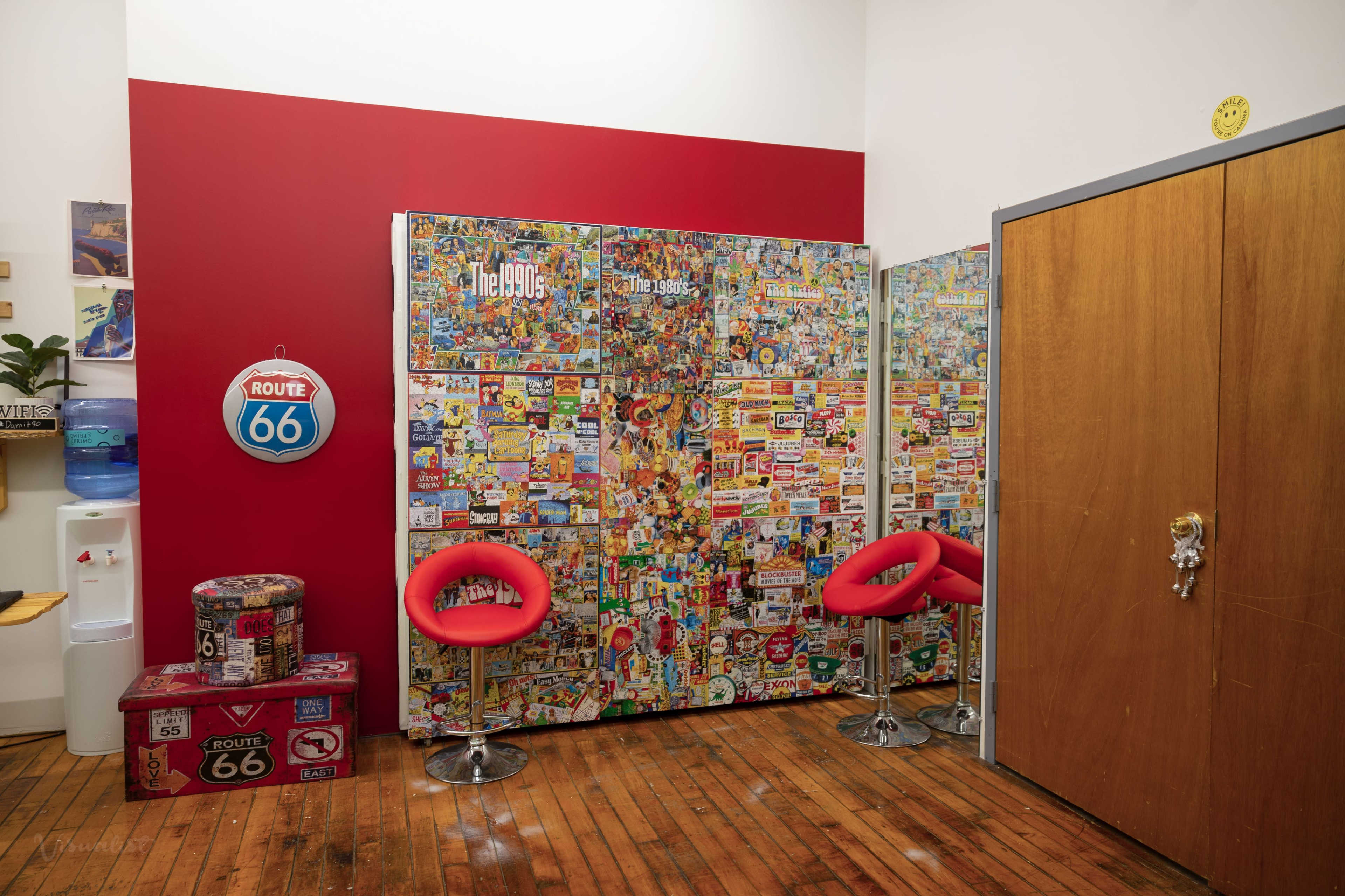 A retro-themed room with a wall covered in colorful stickers, two red chairs, and a wooden door.