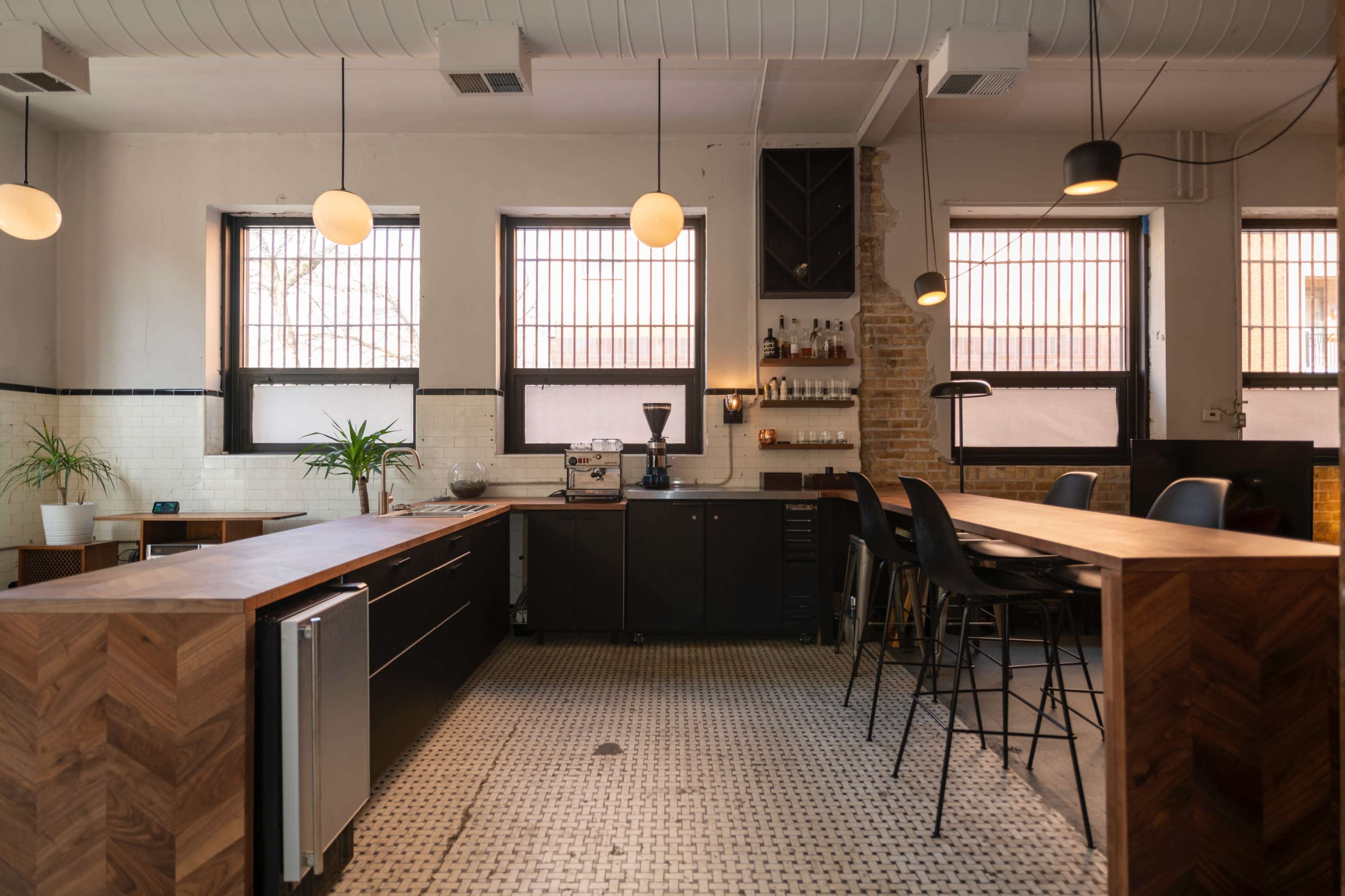 A modern kitchen with wooden countertops, black cabinetry, and a coffee machine, featuring large windows that allow natural light to enter.