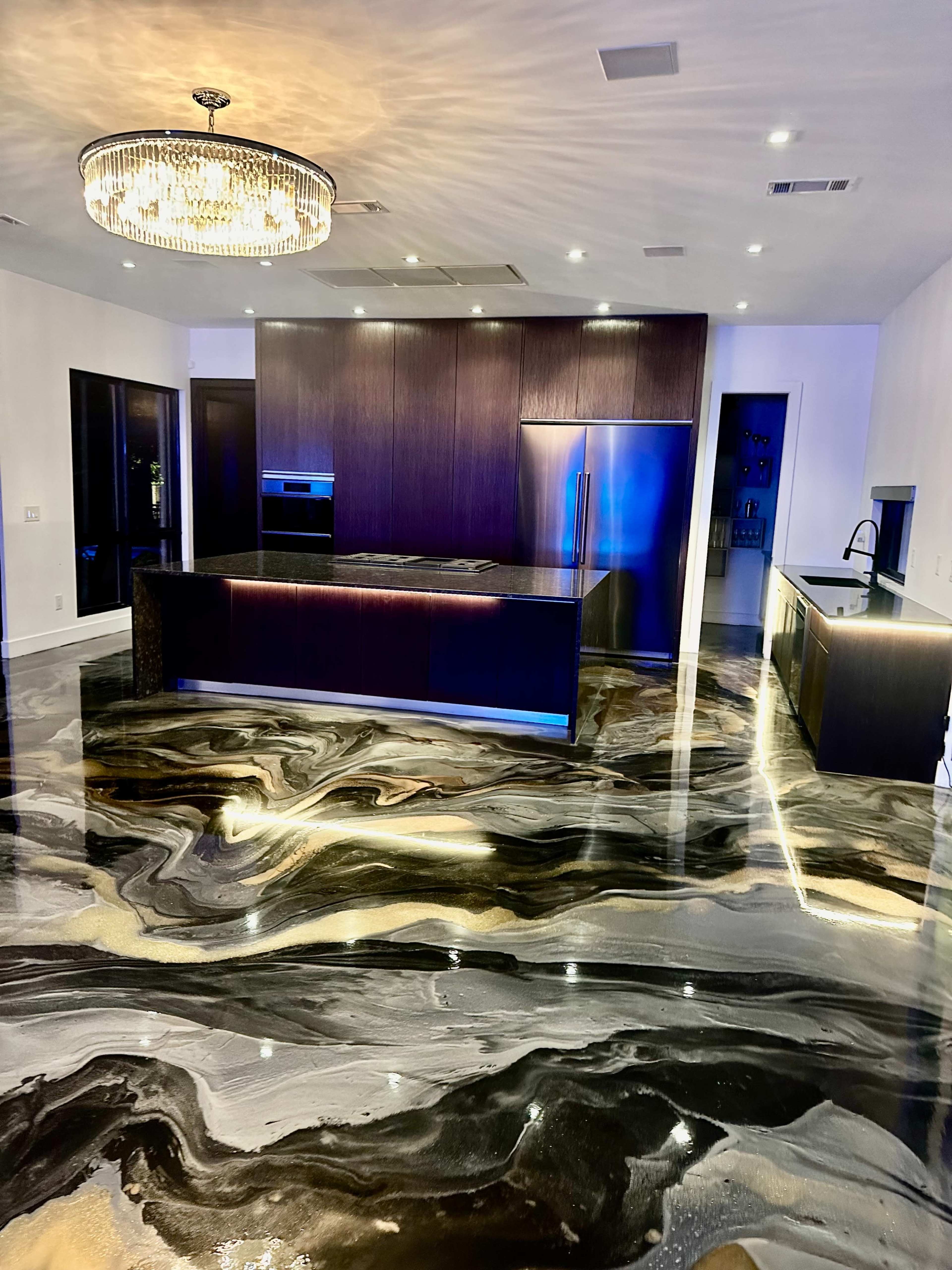 The image shows a modern kitchen with a large island, sleek cabinetry, and a polished, marble-like floor featuring swirling black, gold, and white patterns.