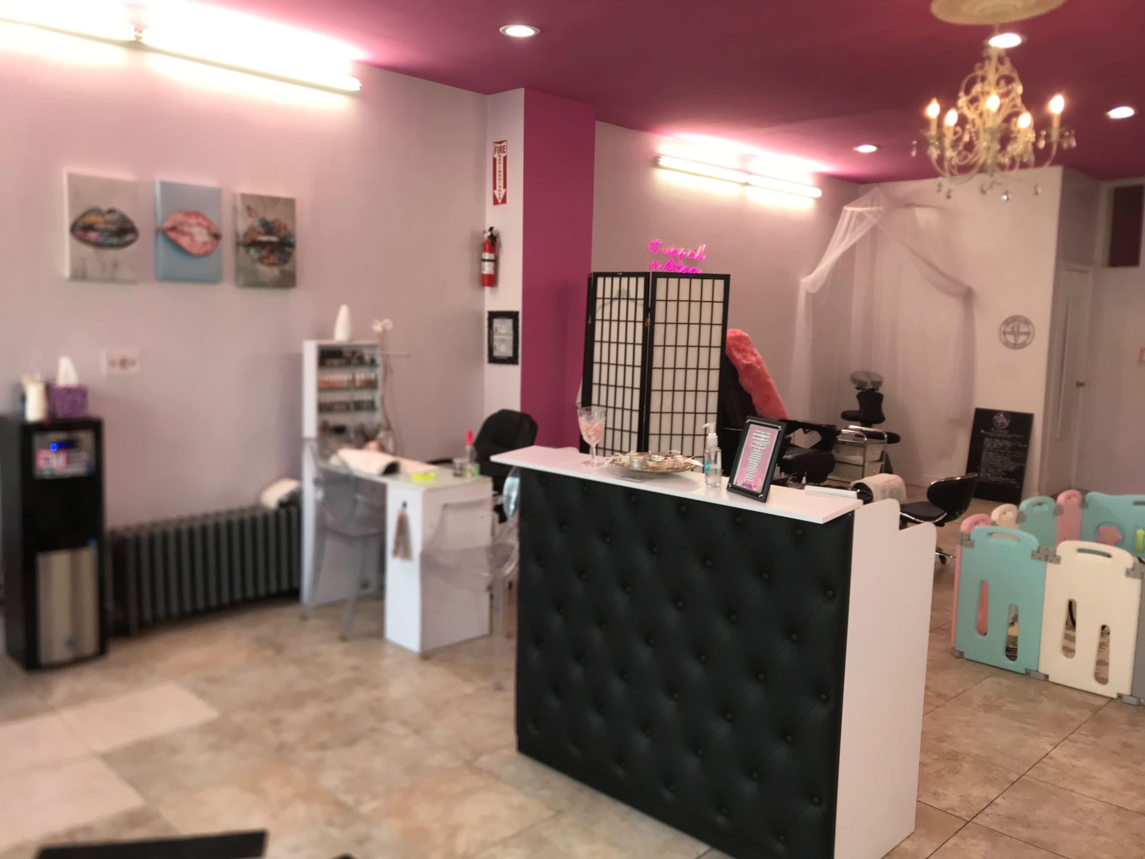 The interior of a beauty salon featuring a reception desk, nail service area, and a chic decor with pink and white accents.