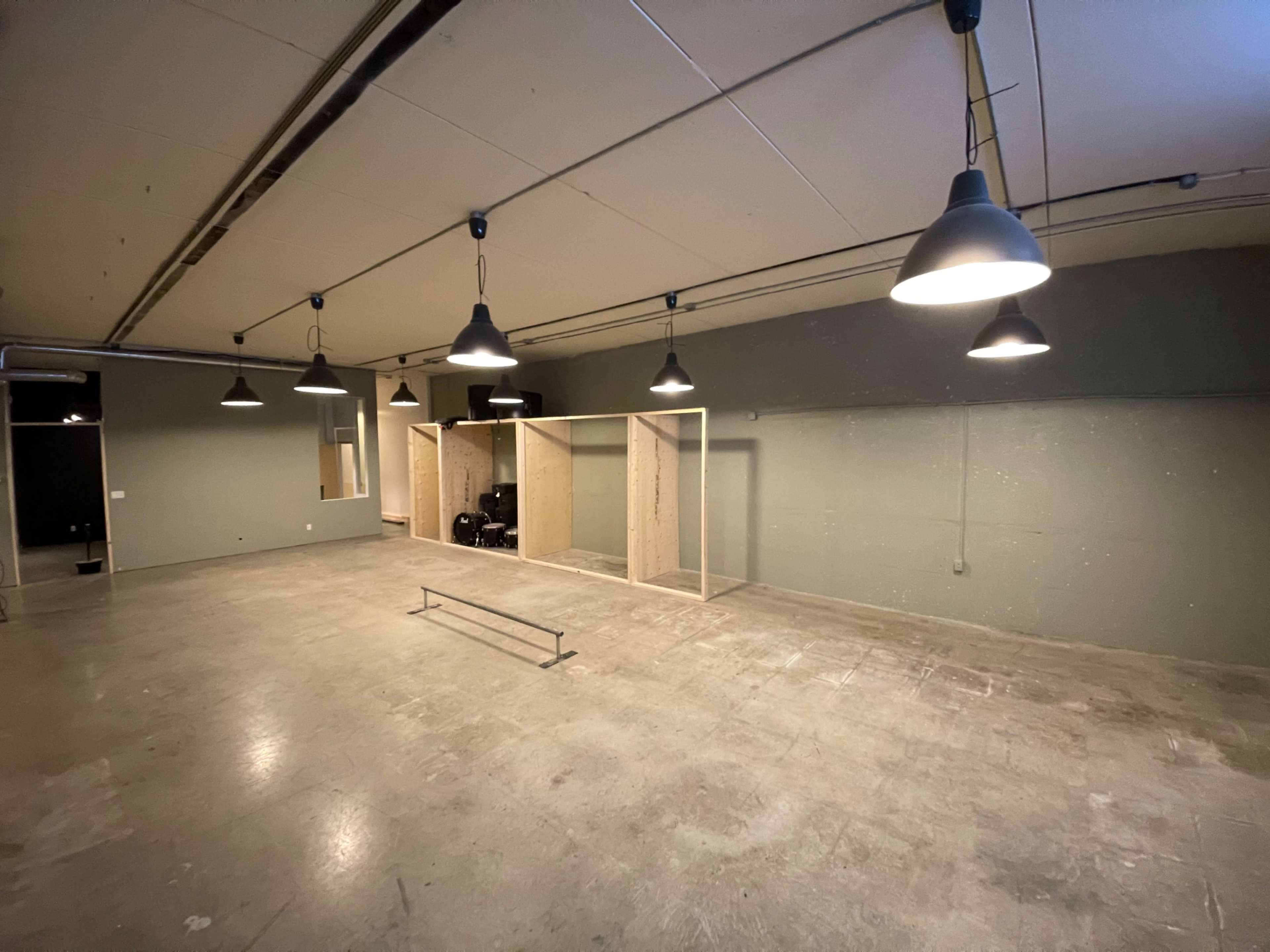 A large, unfinished room with concrete flooring, several pendant lights hanging from the ceiling, and a wooden framework in the center.
