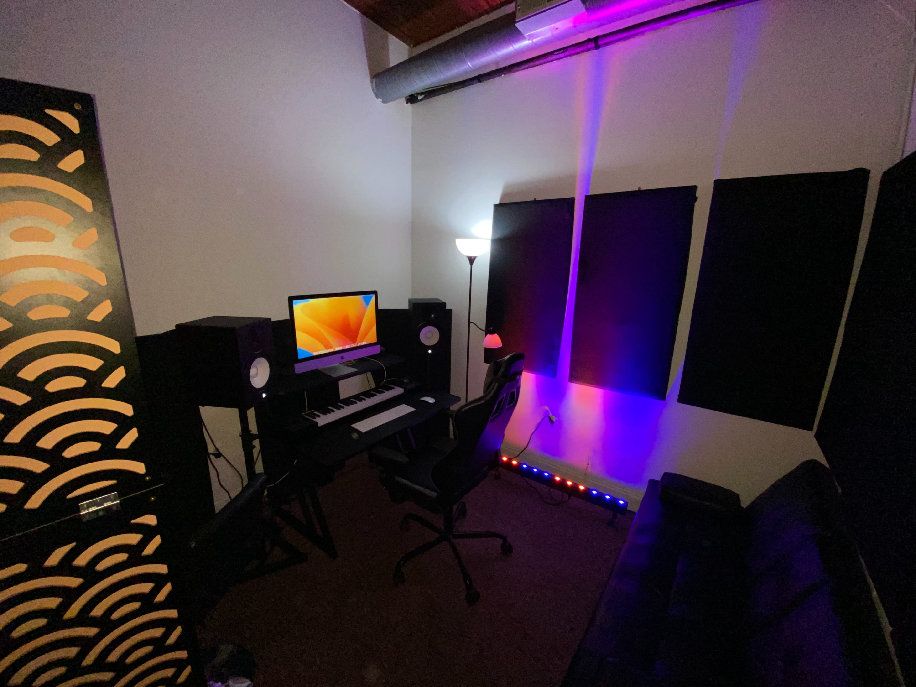 The image shows a music studio featuring a computer workstation with speakers, a keyboard, and colorful lighting accents.