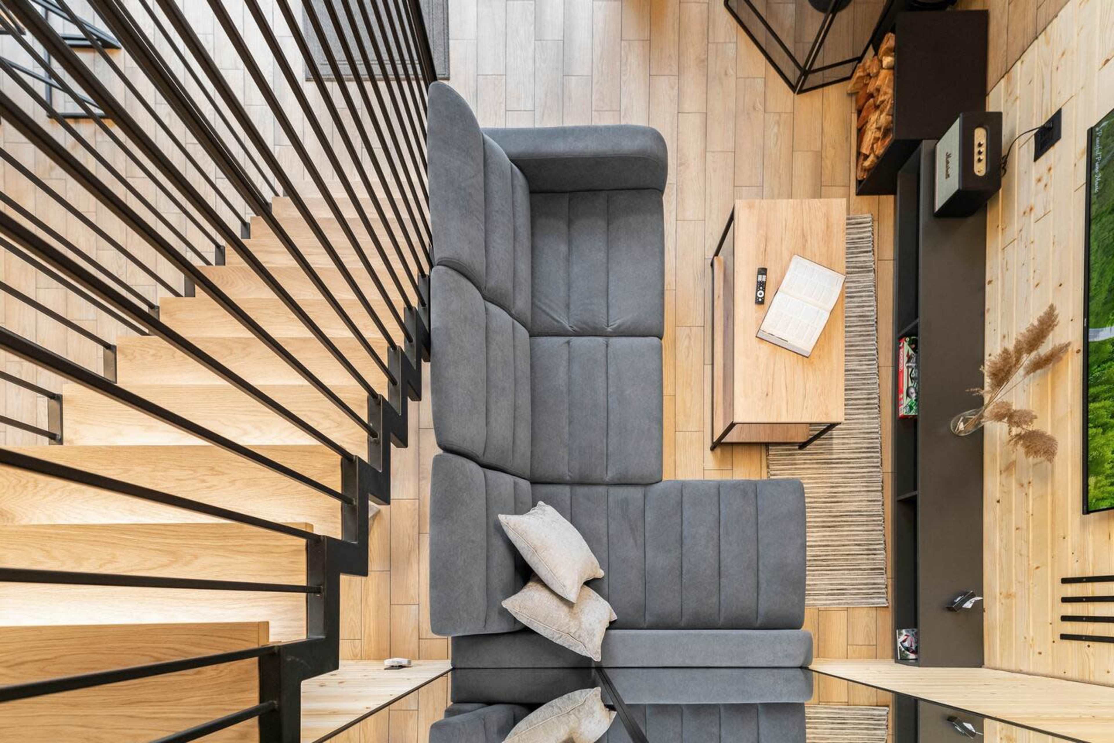 A modern living room with a gray sectional sofa, a wooden coffee table, and a staircase with black railings.