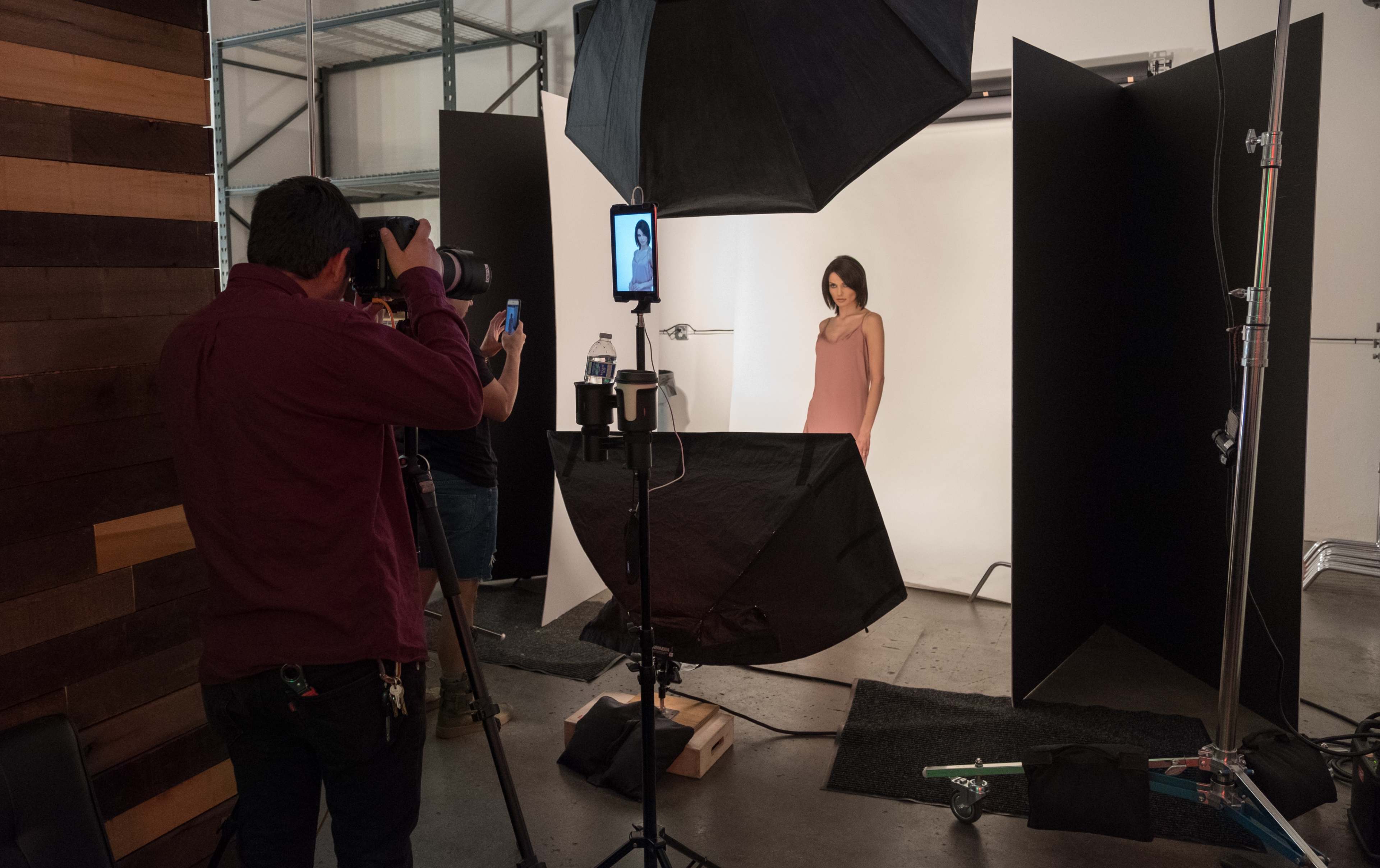 A photographer captures a model in a studio setting, with lighting equipment and backdrops arranged to create a professional photo shoot.