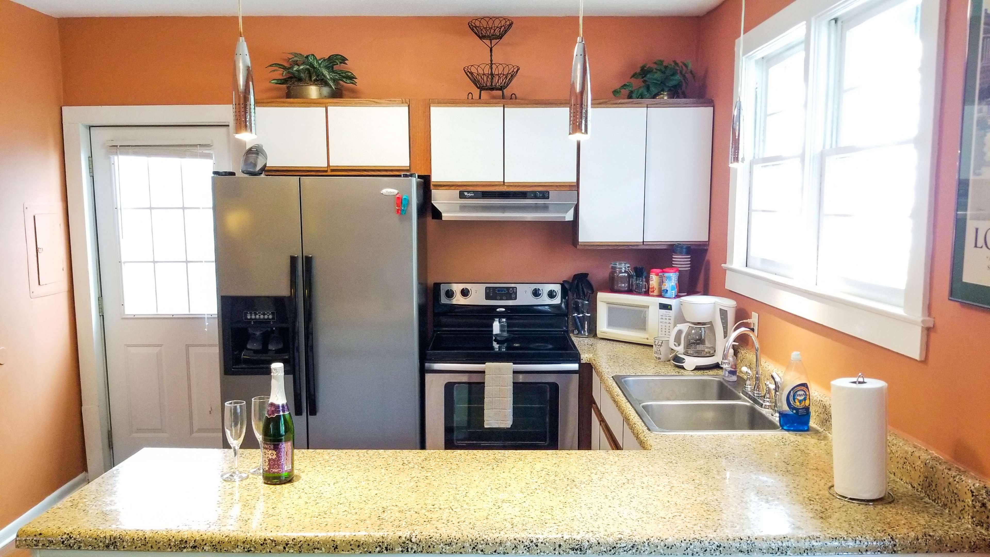 A modern kitchen features a granite countertop, stainless steel appliances, and orange walls with white cabinets.