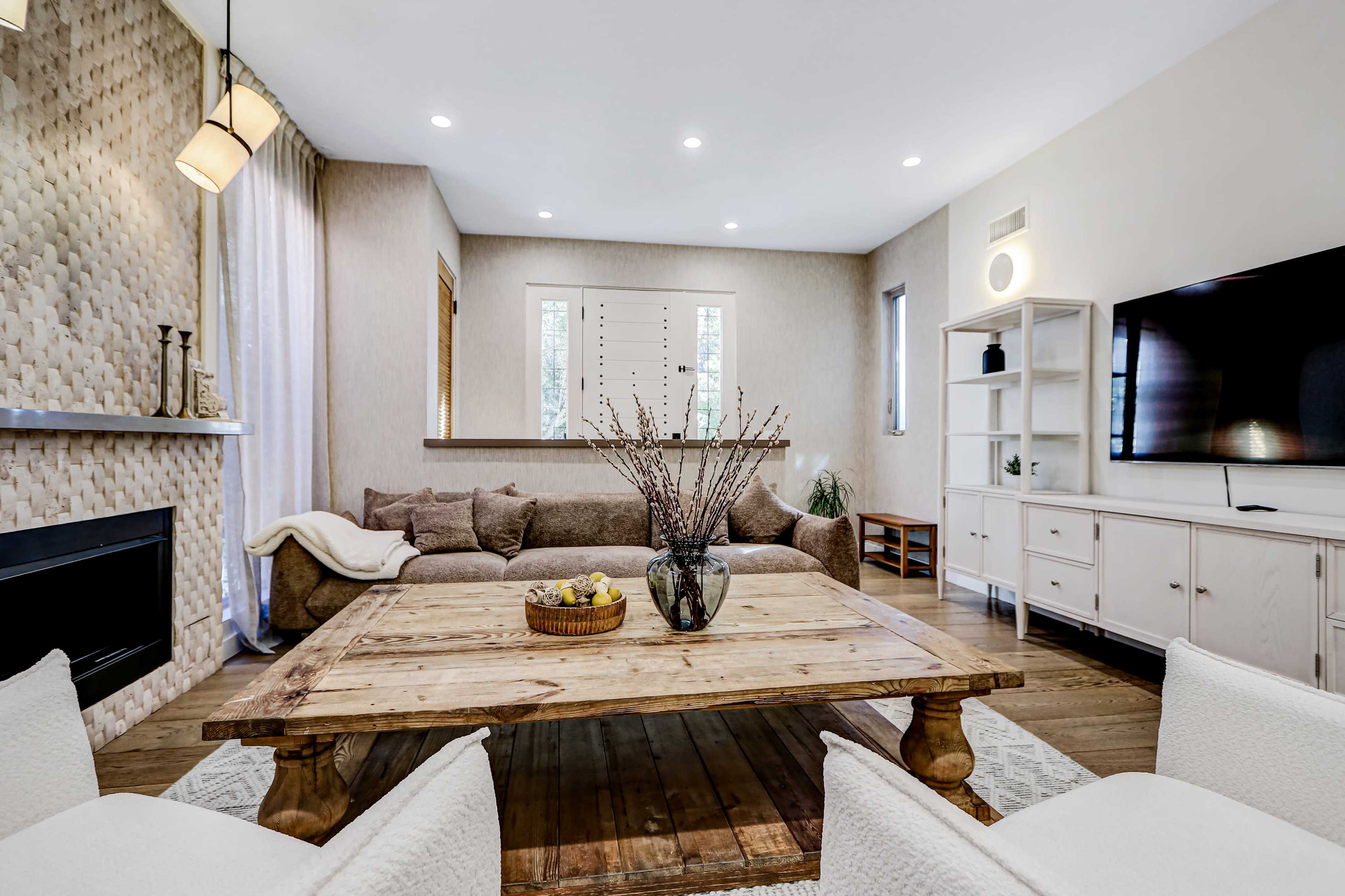 The image shows a modern living room with a large wooden coffee table, a sectional sofa, and a television mounted on the wall.