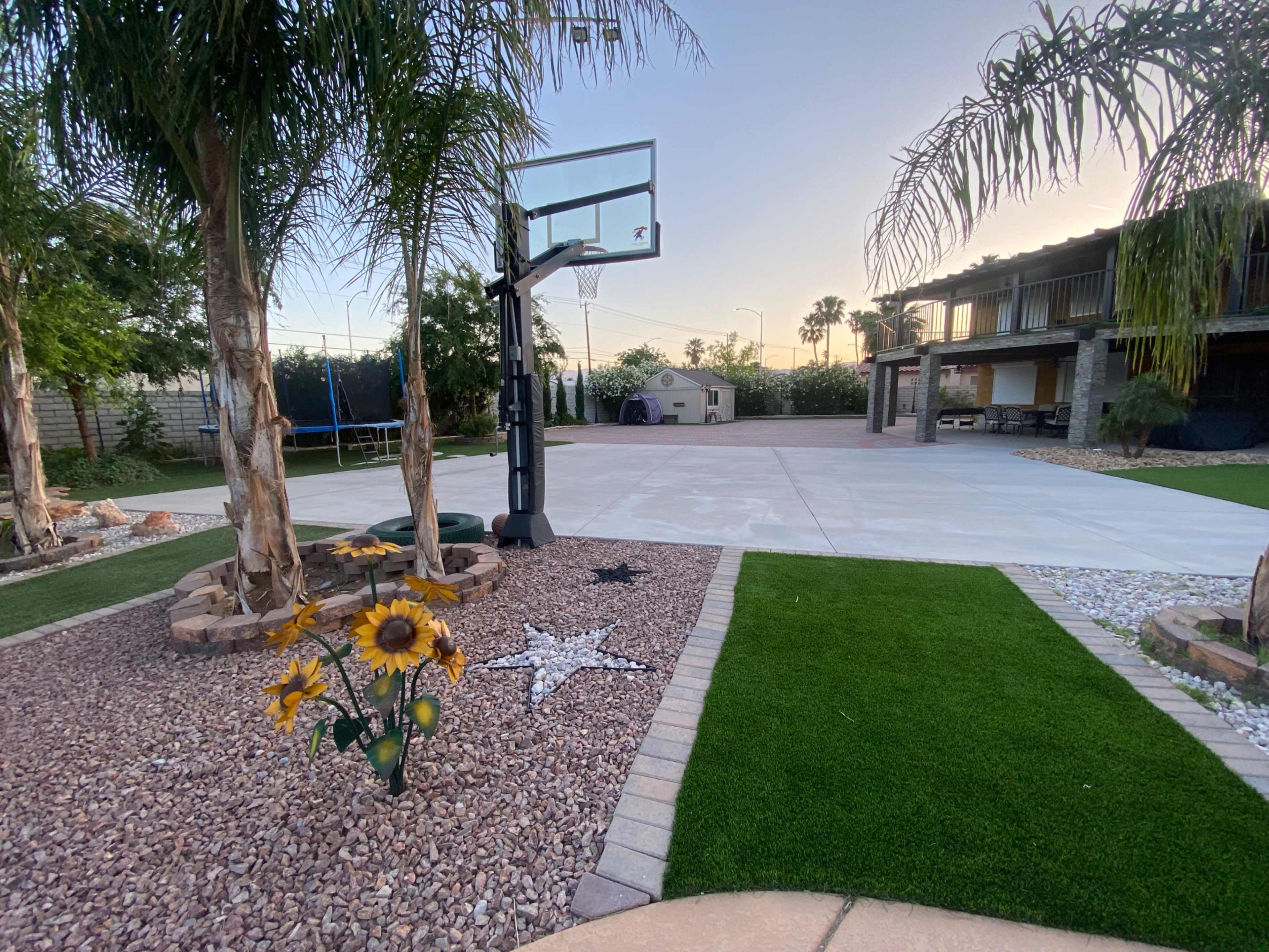 The image showcases a spacious backyard with a basketball hoop, a manicured lawn, desert landscaping, and a large concrete area.