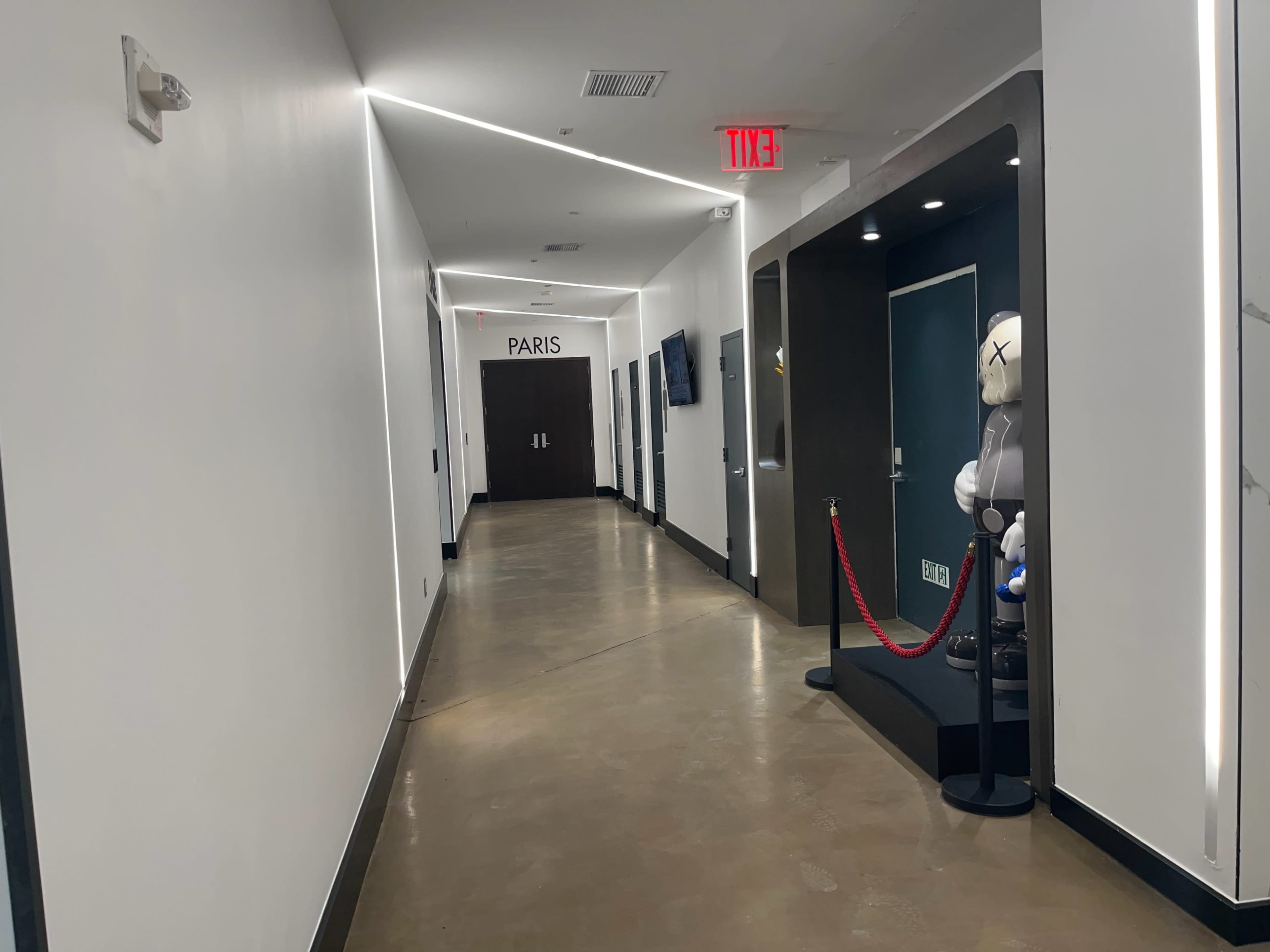 The hallway features a sign labeled "PARIS," with doors on either side and a decorative figure next to a roped-off area.