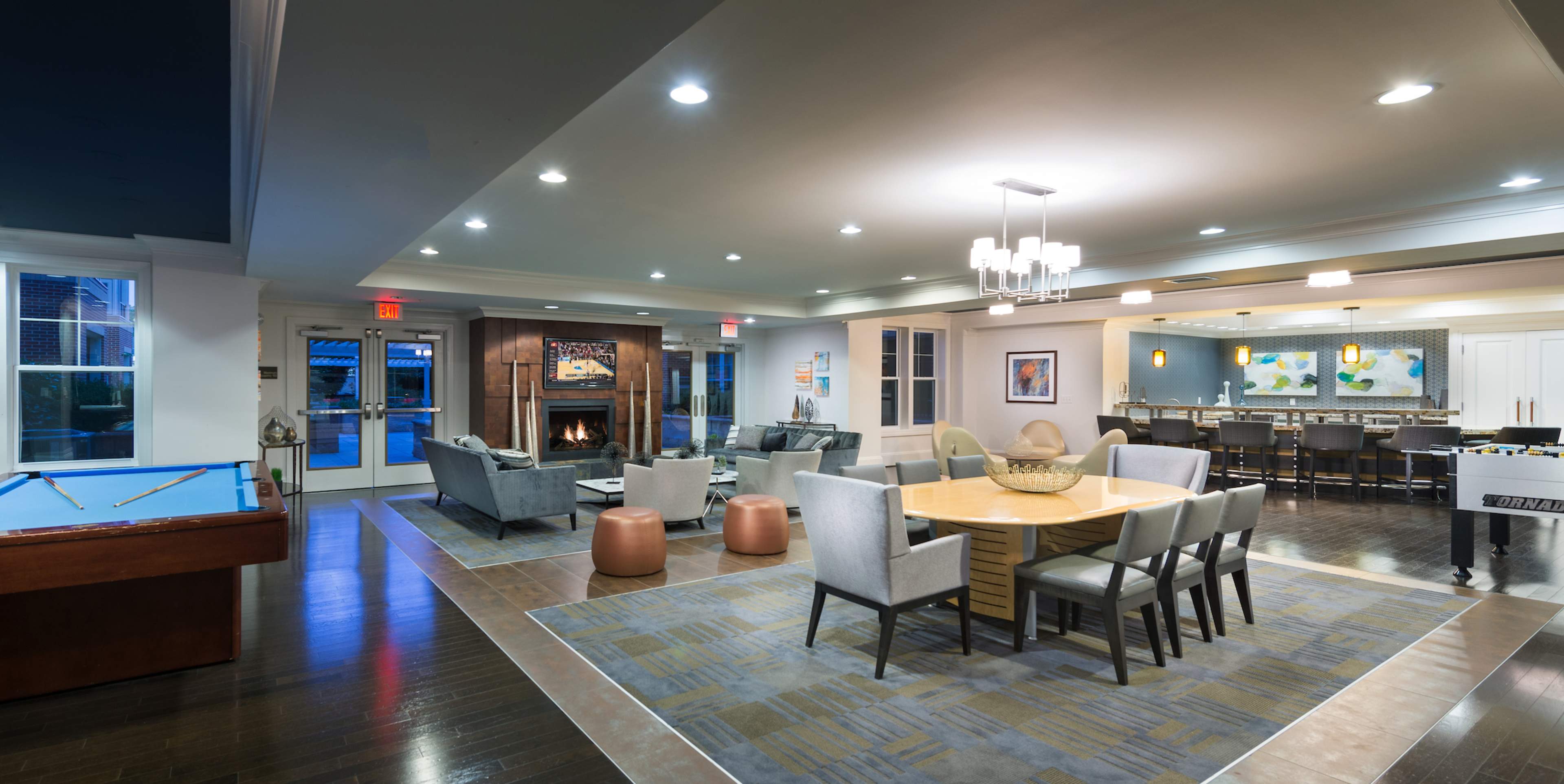 A spacious common area featuring a dining table, comfortable seating, a fireplace, and a pool table, with modern decor and ambient lighting.