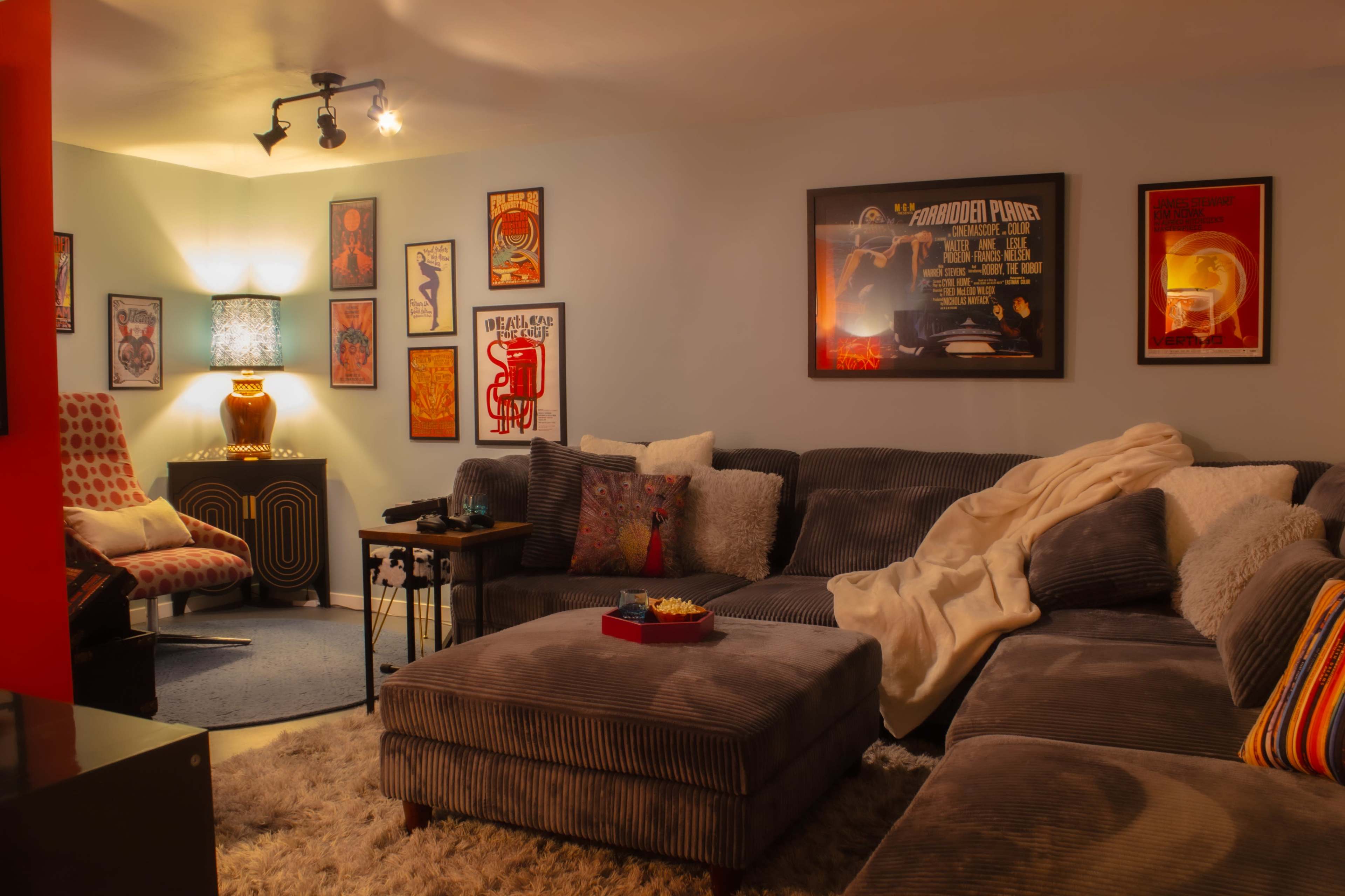 The living room features a large sectional sofa, a coffee table with snacks, and colorful, vintage-style posters adorning the walls.