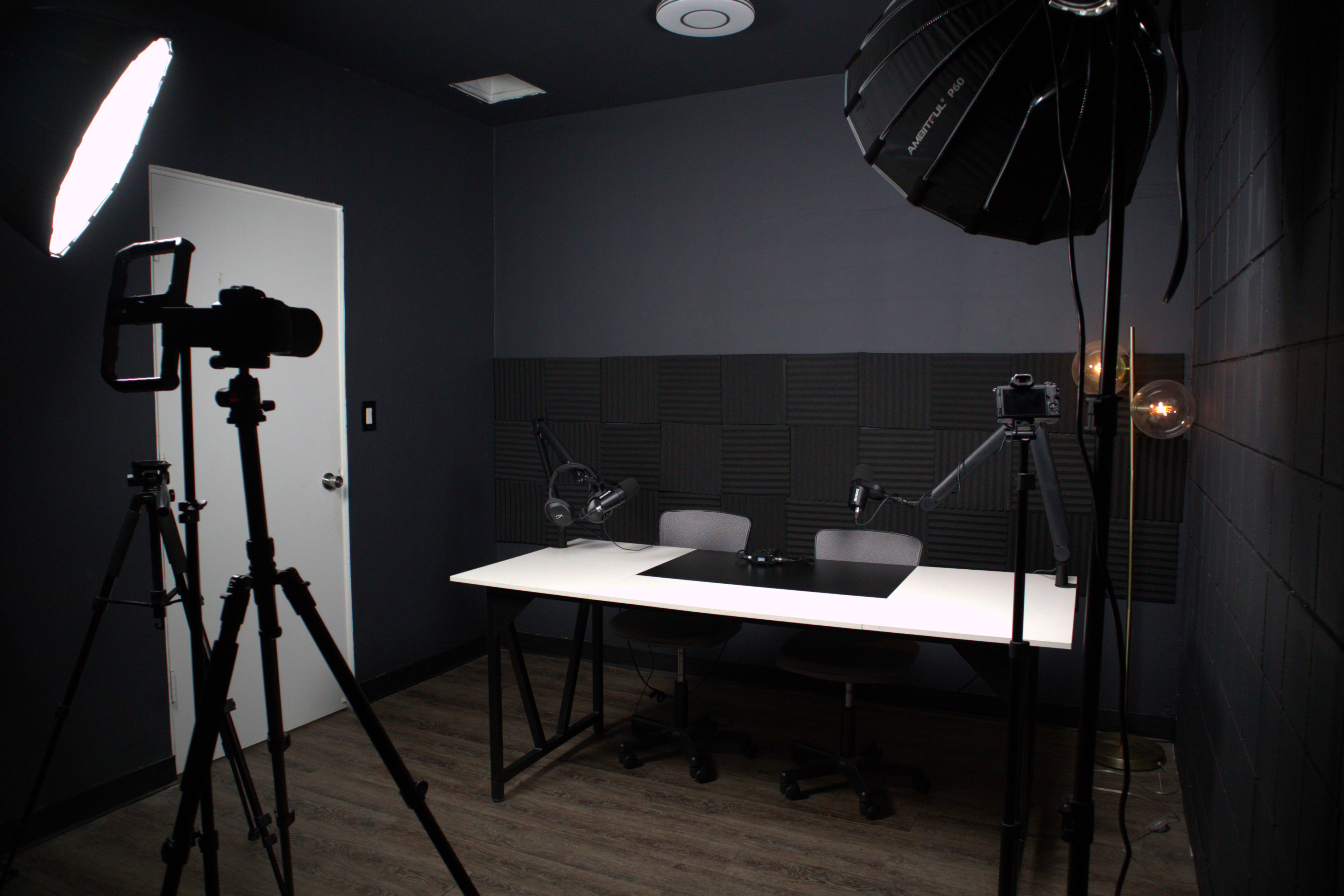 A dimly lit recording studio with two chairs and a table, equipped with lighting and audio equipment.