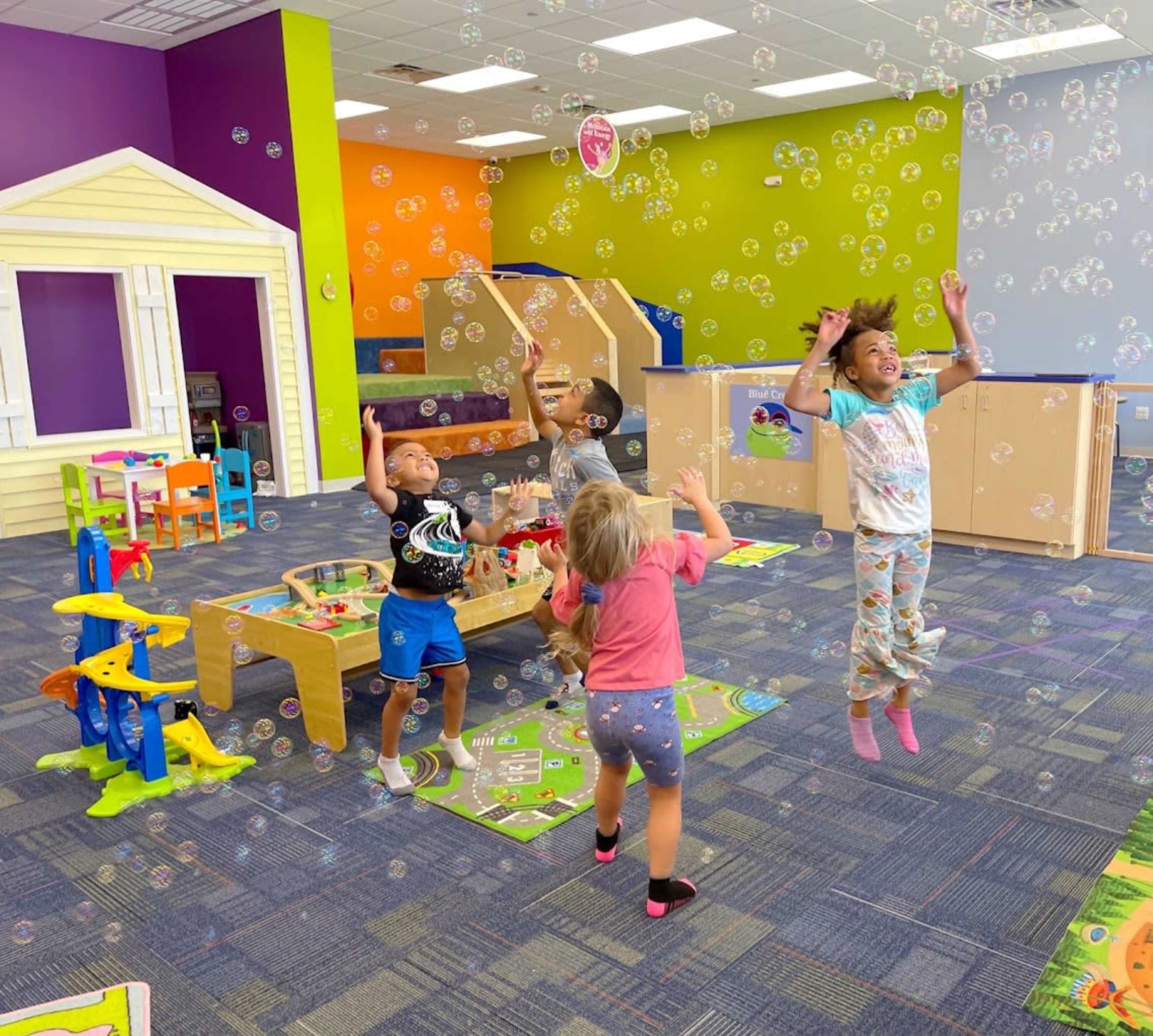 A group of children playfully jump in a colorful indoor play area filled with bubbles.