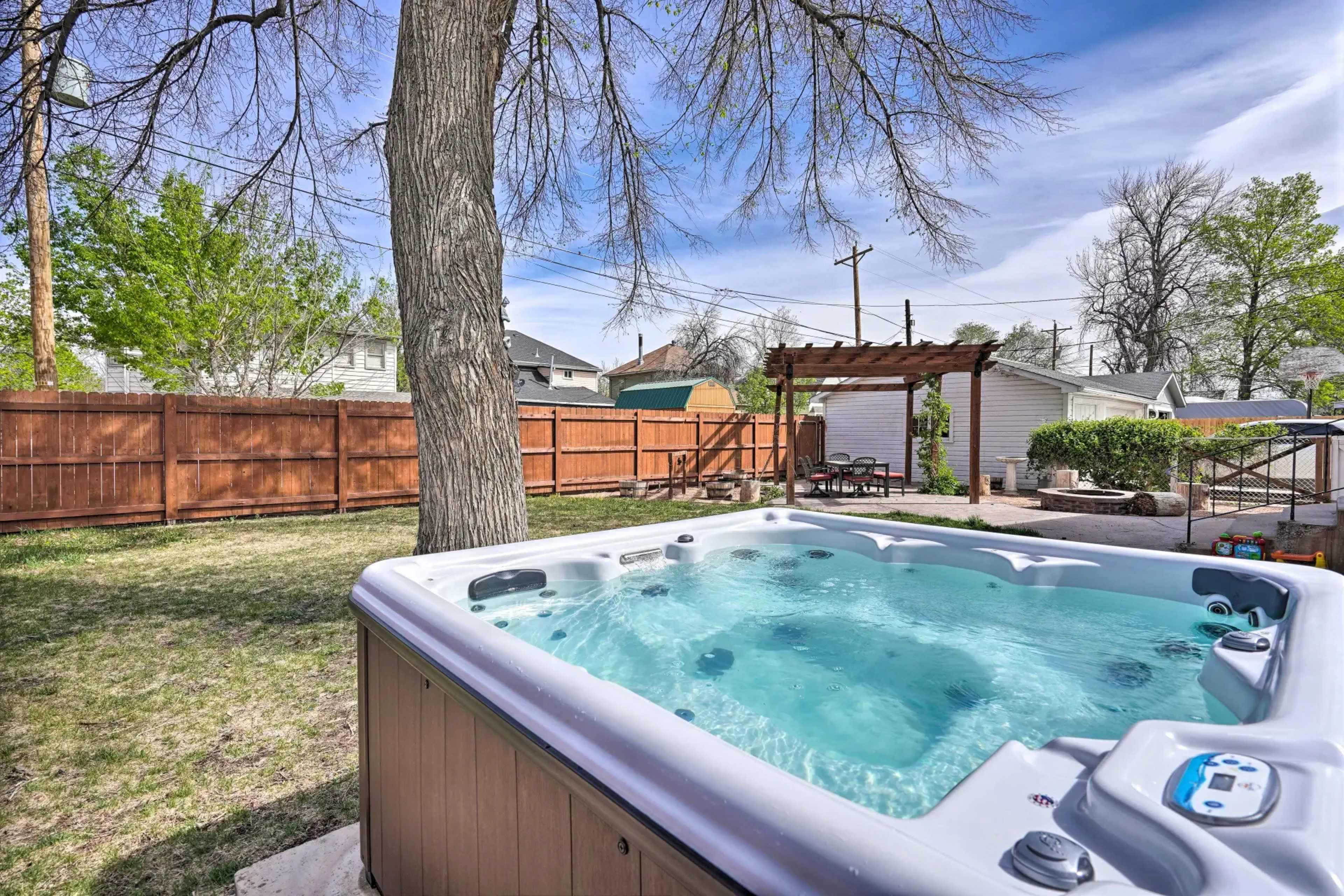 A hot tub is positioned in a backyard with a wooden fence and trees in the background.