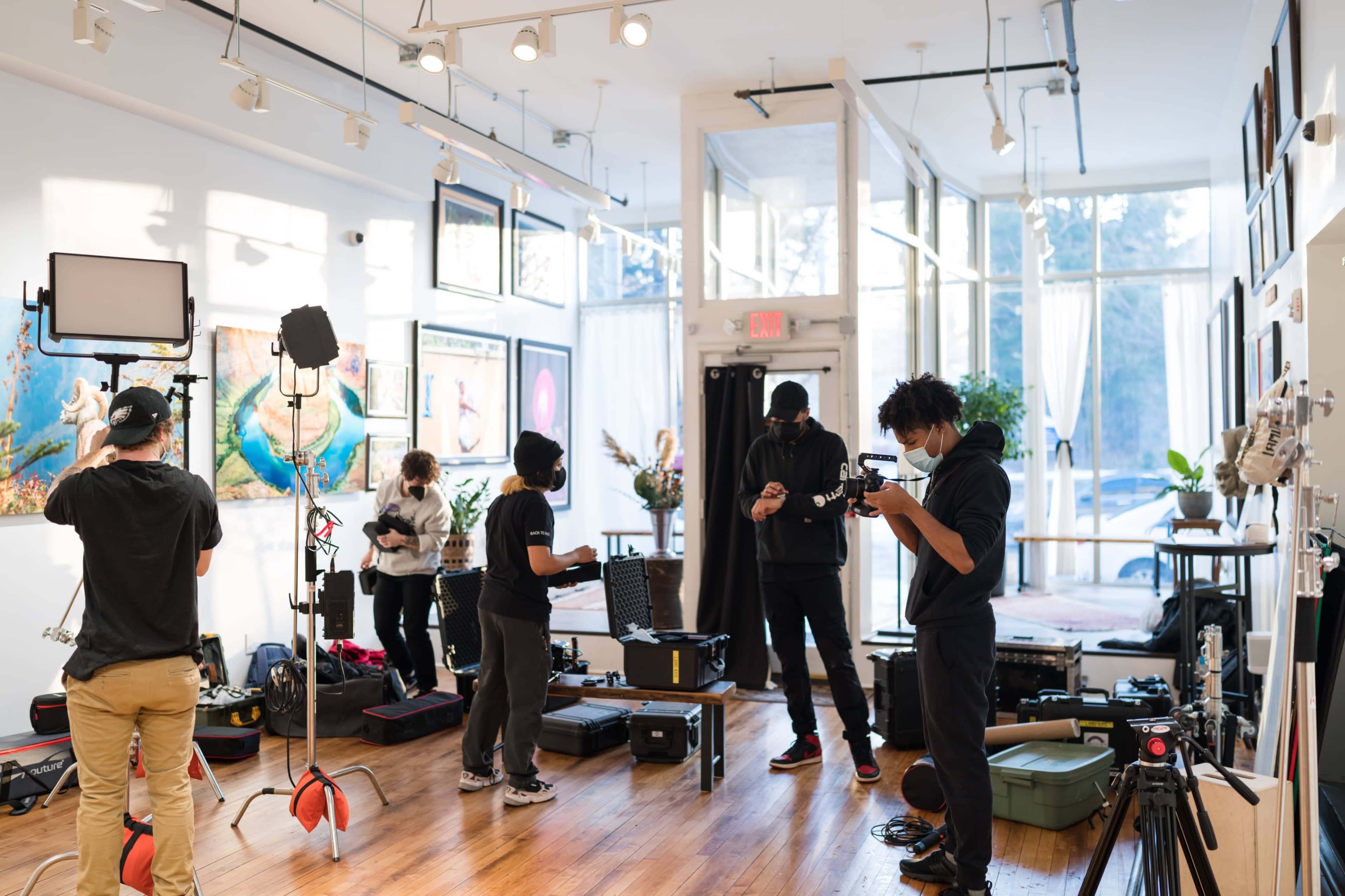 A film crew sets up equipment inside a bright studio, preparing for a shoot amidst various lighting and camera gear.