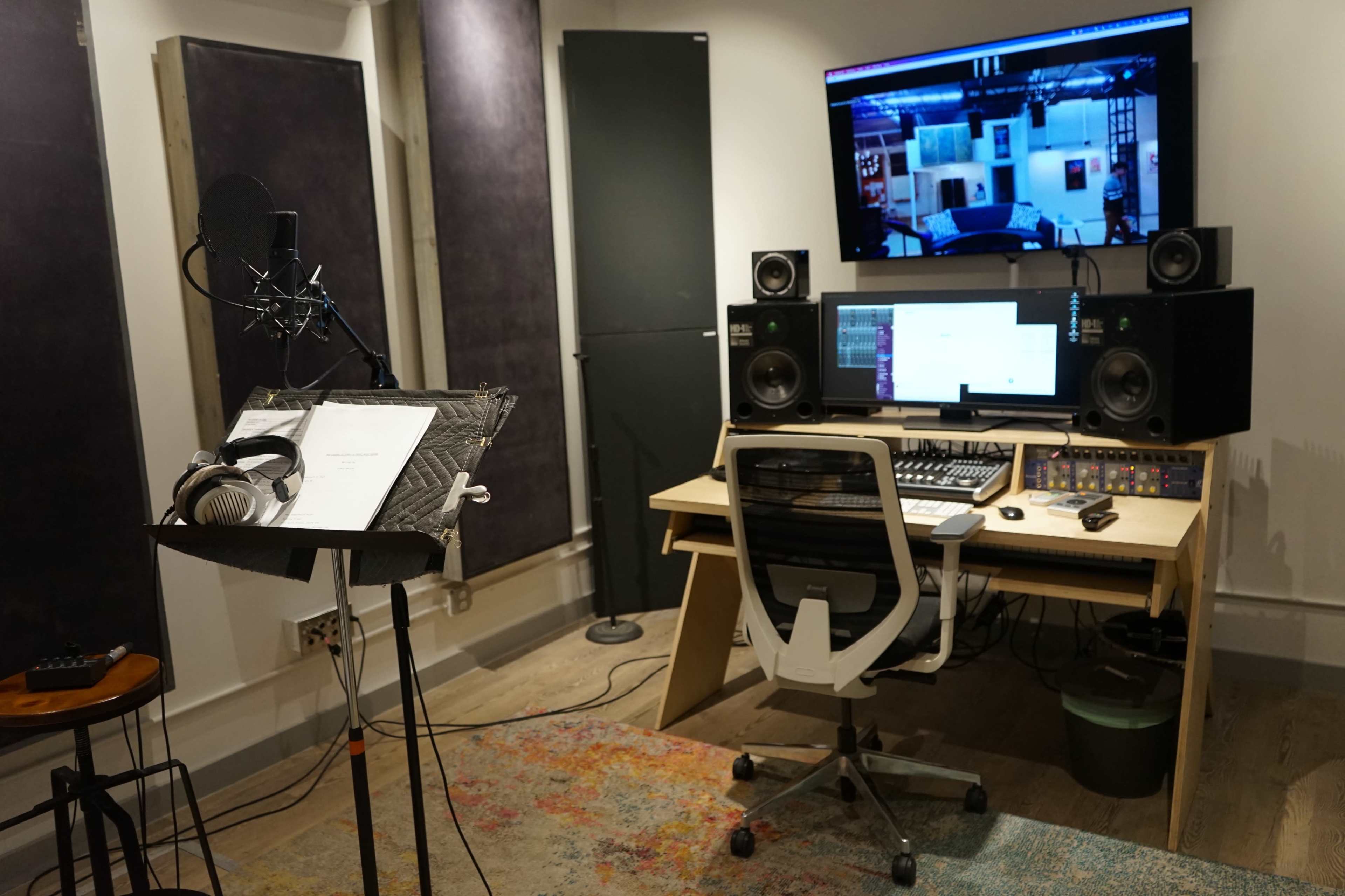 A recording studio featuring a microphone, music stand with sheet music, a computer setup, and audio equipment.