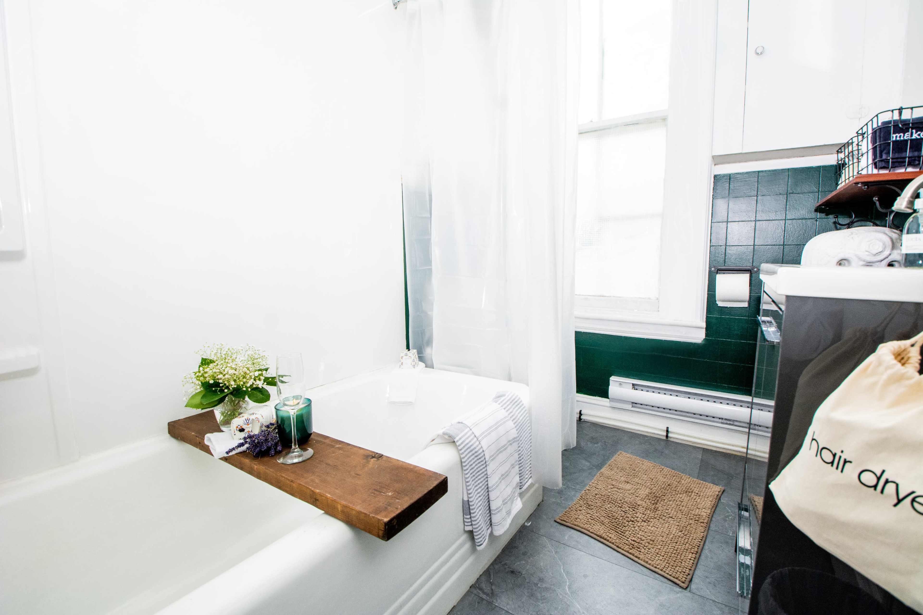 A modern bathroom featuring a bathtub with a wooden tray, a shower curtain, and green tile accents.