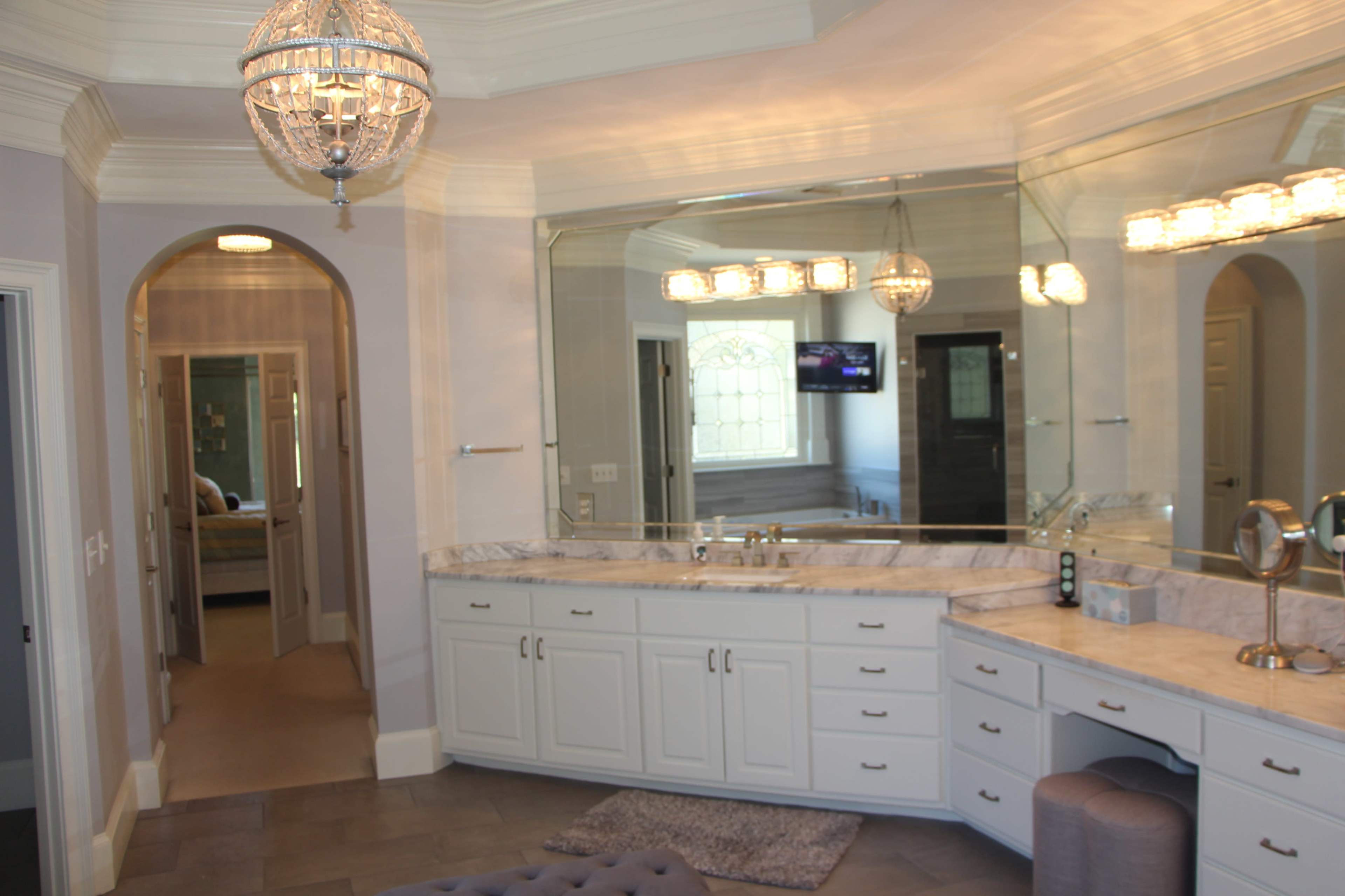 The image shows a spacious bathroom featuring a double vanity with a marble countertop, a large mirror, and a chandelier overhead.