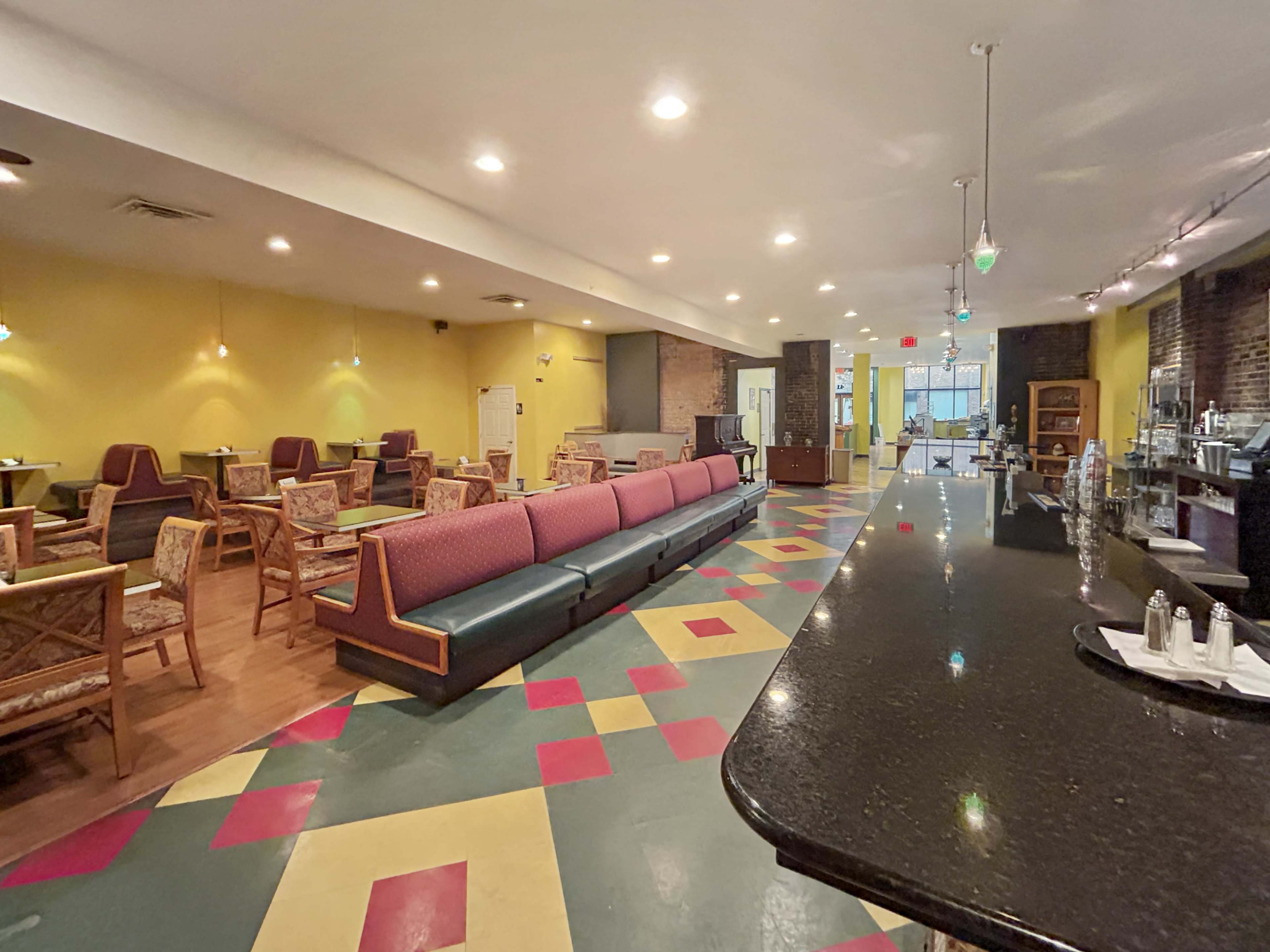 A spacious café with colorful tiled flooring, a long bar counter, and seating areas featuring a mix of chairs and tables.