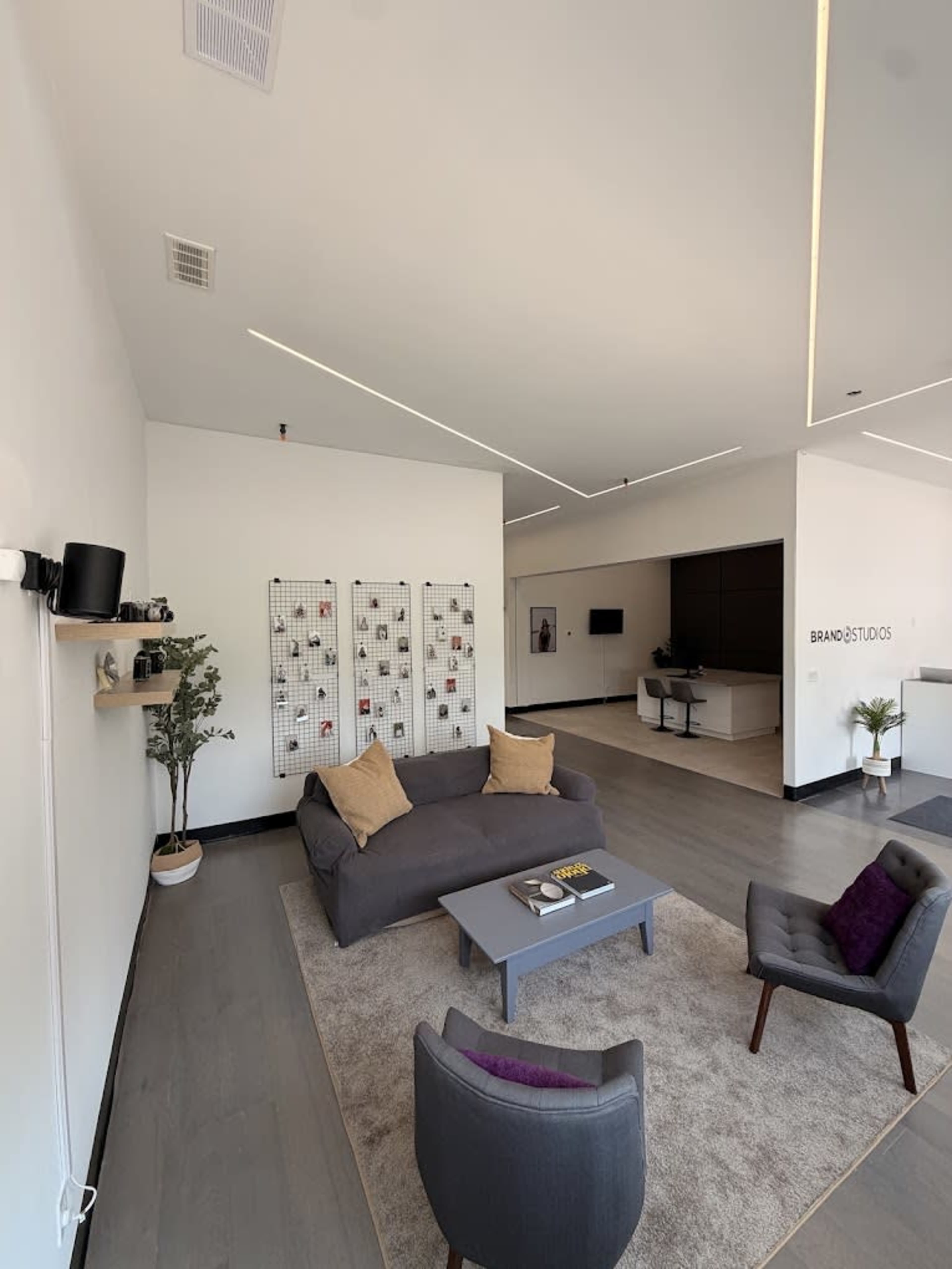 A modern interior space features a gray sofa on a light carpet, surrounded by a small table and two chairs, with minimalist decor and a wall-mounted display.