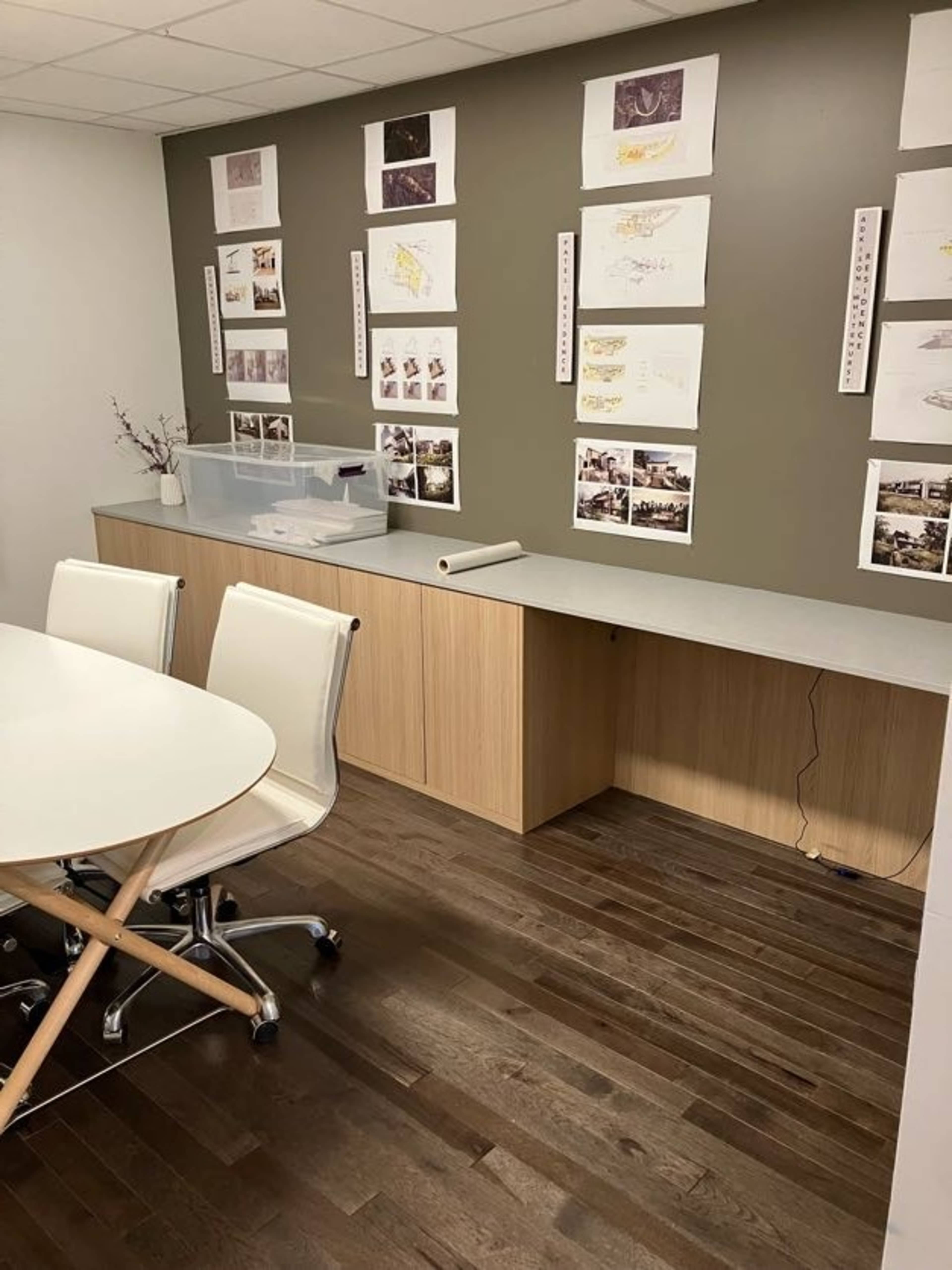 A modern meeting room with a round table and white chairs, featuring a wooden floor and walls adorned with various paper displays.