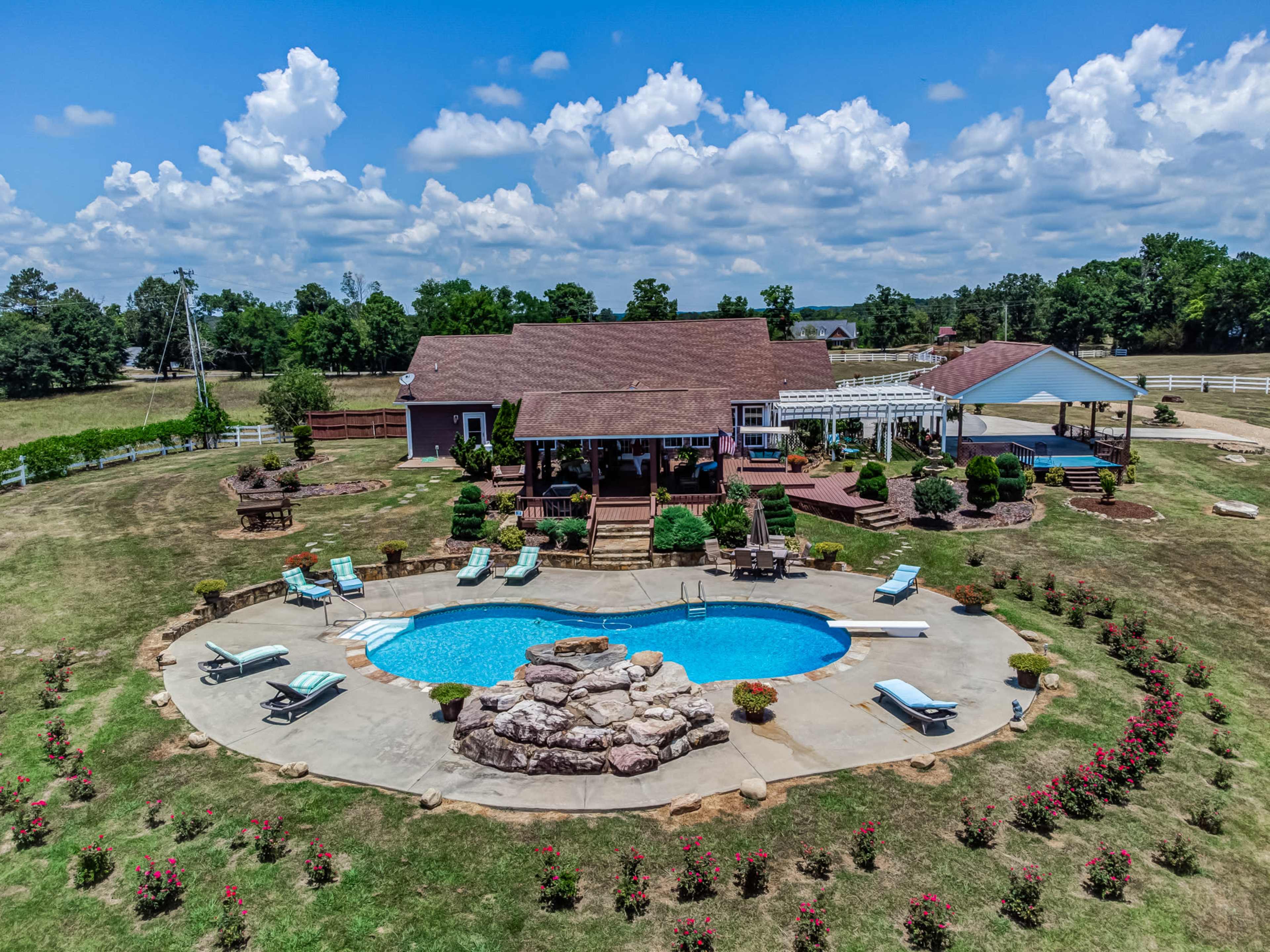 The image shows a spacious backyard with a house, a swimming pool surrounded by rock landscaping, and lounge chairs arranged around the pool.
