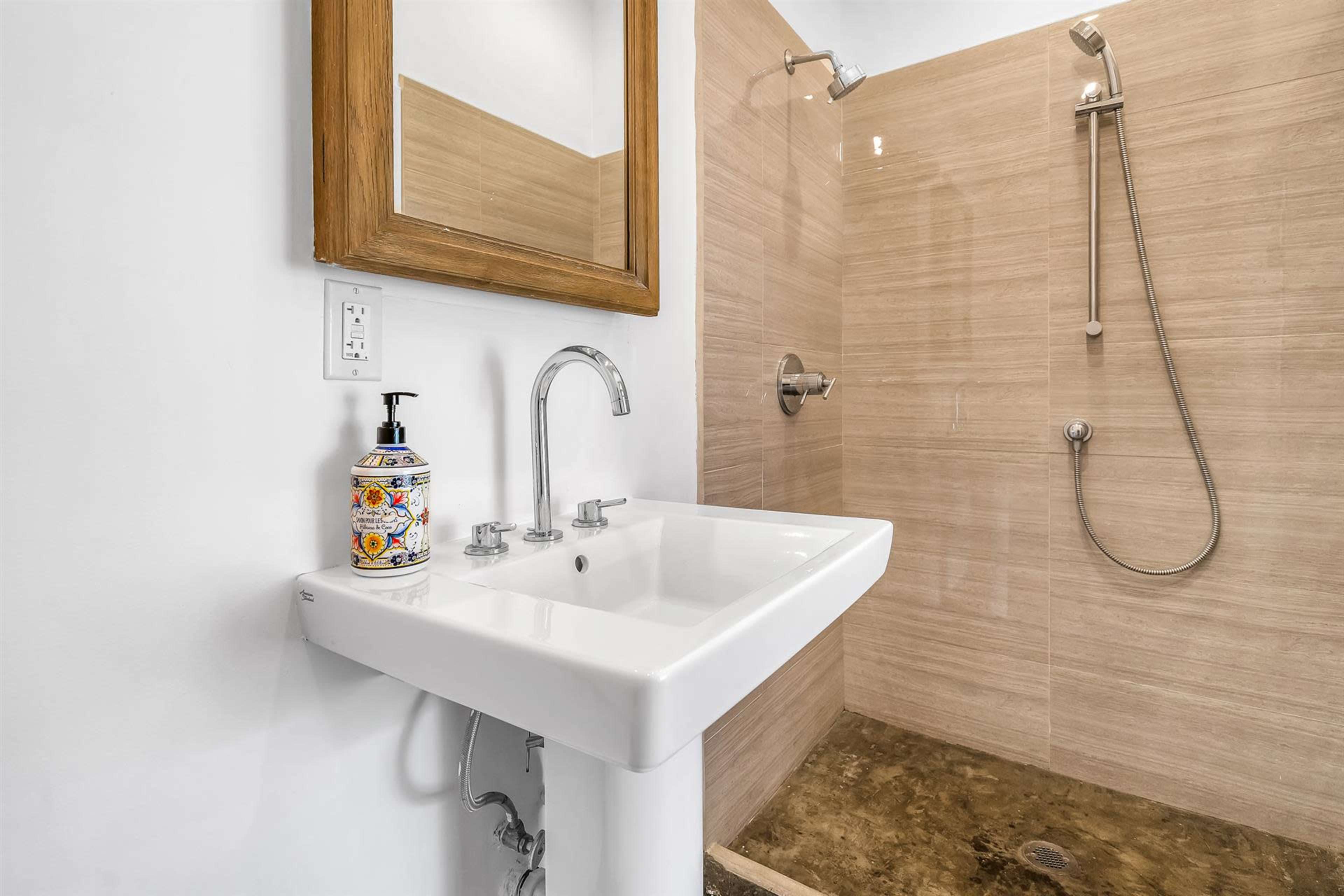 A clean bathroom space featuring a sink with a decorative soap dispenser and a glass-enclosed shower with beige tiled walls.