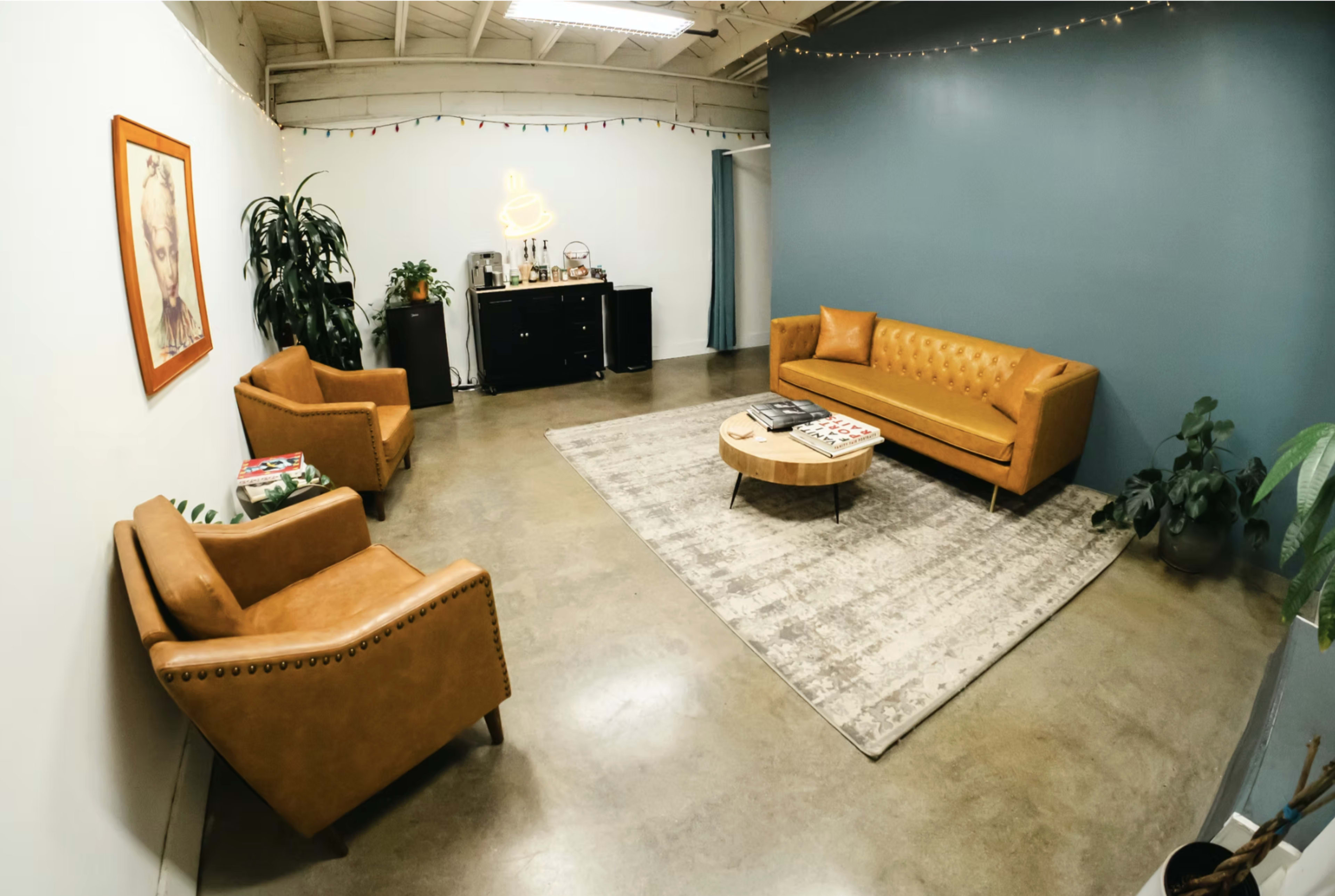 The image shows a modern, minimalist lounge with orange leather furniture, a round coffee table, and a wall adorned with string lights.