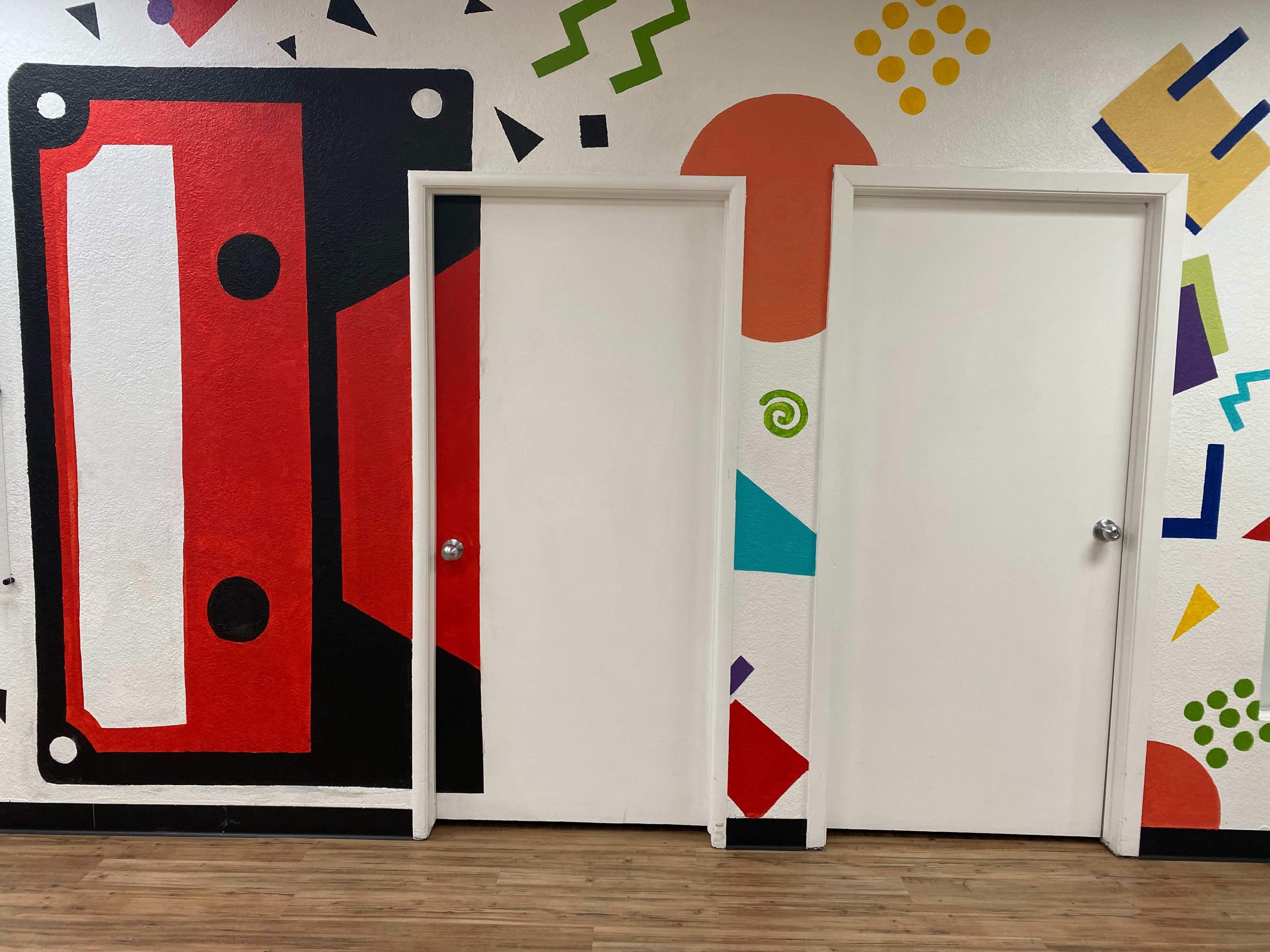The image shows a colorful mural featuring a large red cassette tape on the left, adjacent to two plain white doors.