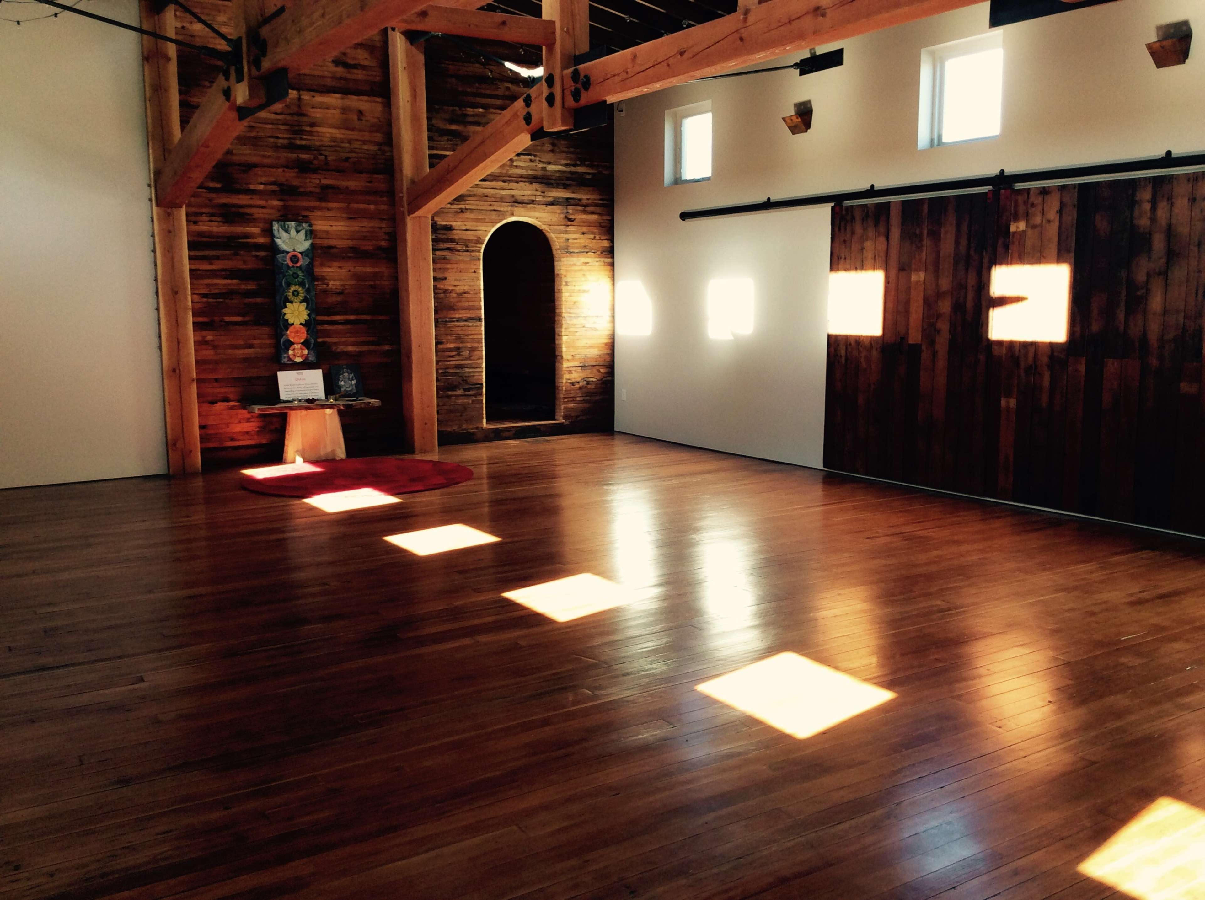 The interior features wooden beams and a polished floor, illuminated by sunlight casting square patterns on the surface.