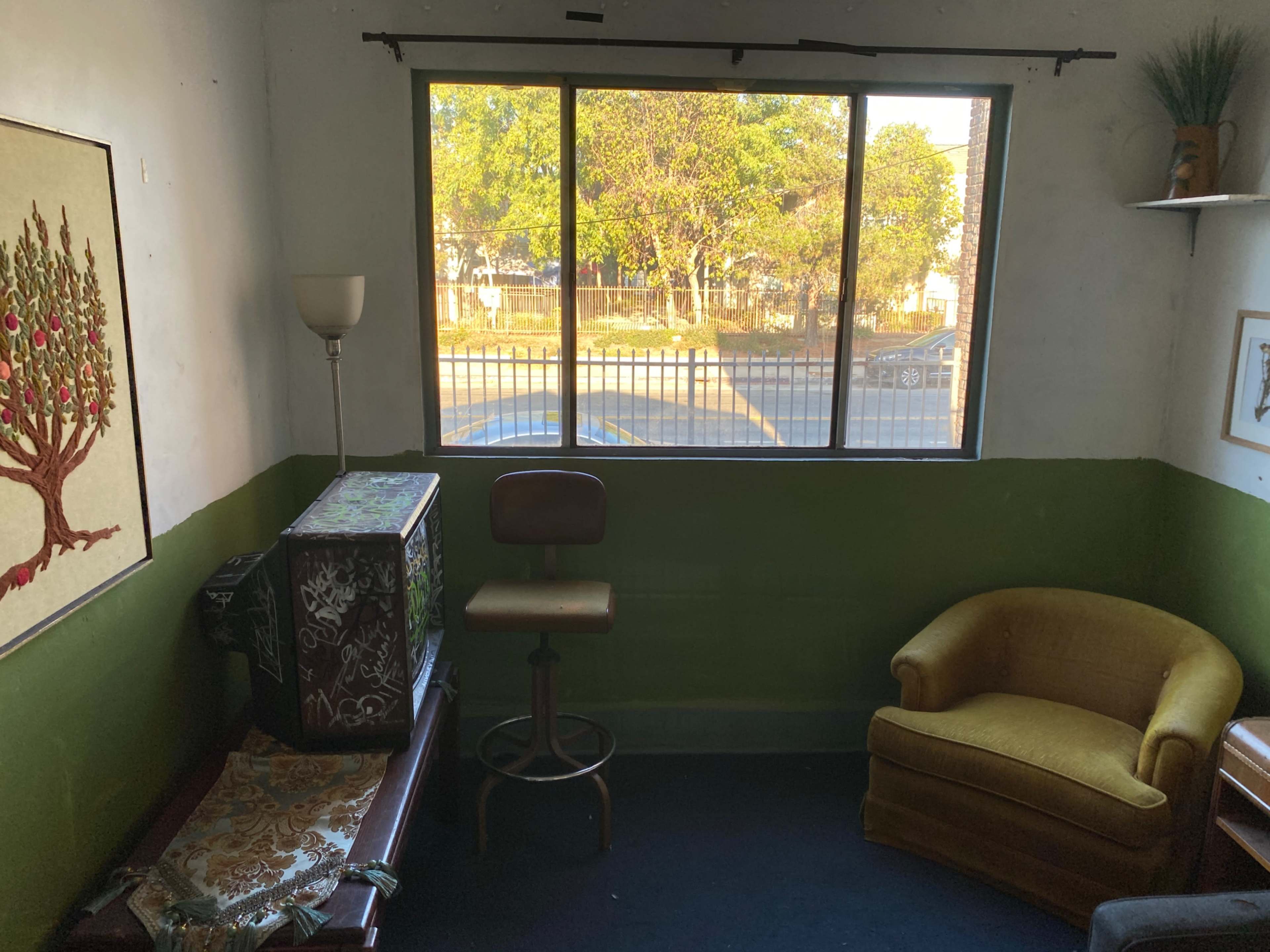 A small room with a green and white color scheme, featuring a window, a chair, a wooden table, and a decorative piece on the wall.