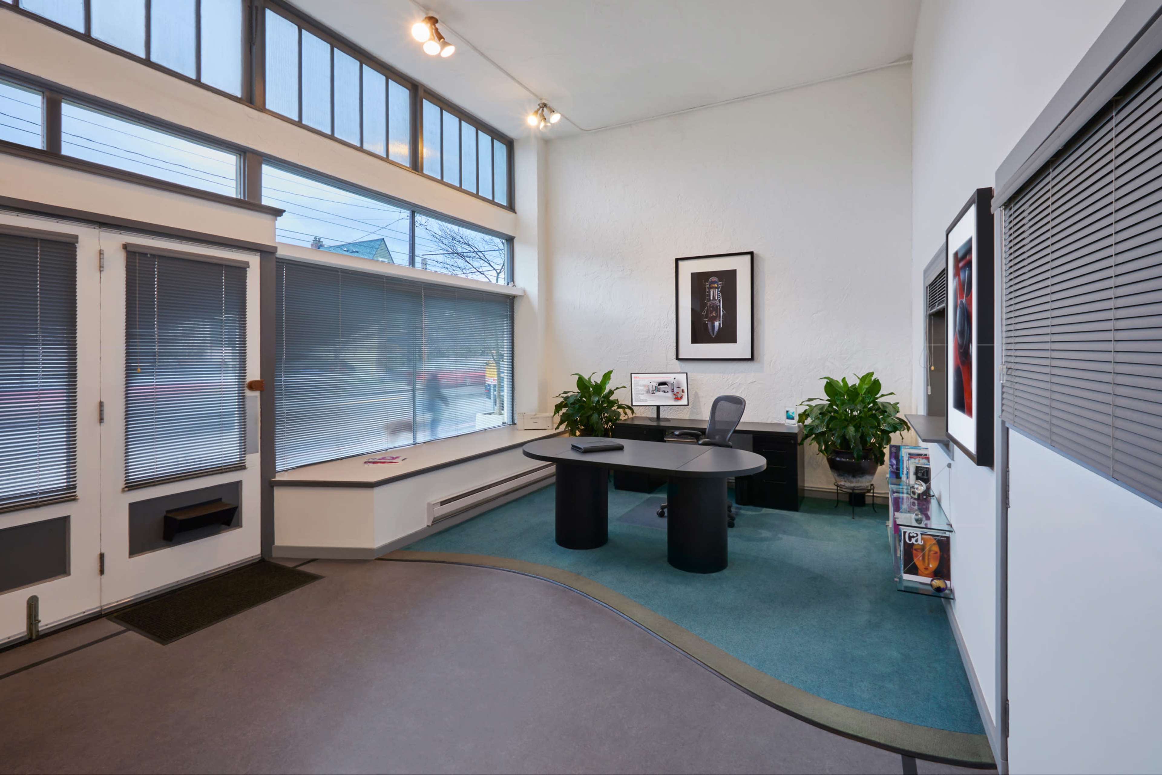 A modern office reception area with a curved black desk, green plants, and large windows allowing natural light.